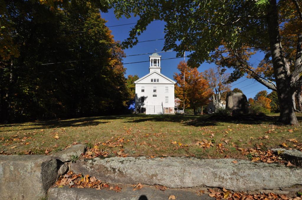 White church with a steeple on a sunny autumn day, surrounded by colorful trees.