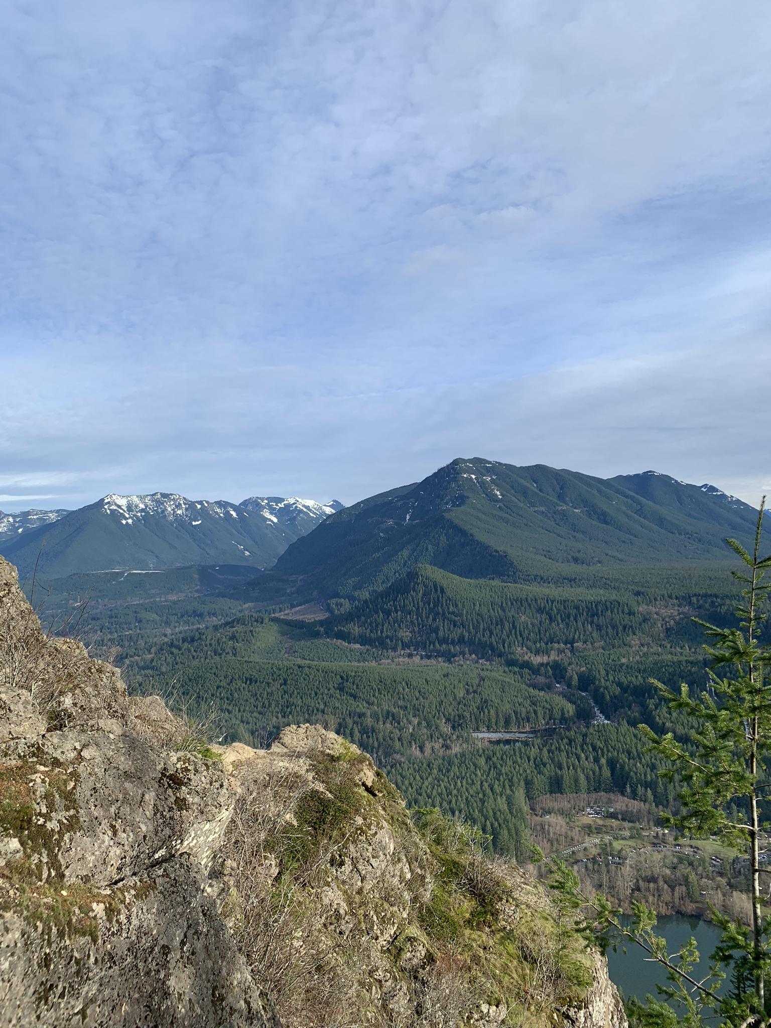 Clear day view of distant mountains and a vast forest from a rocky cliff.