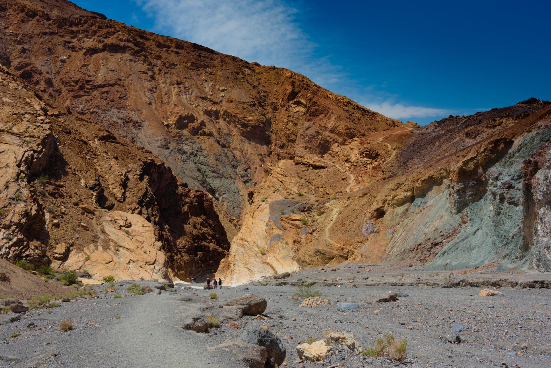 Wide canyon floor with distant hikers and towering, colorful rock walls.