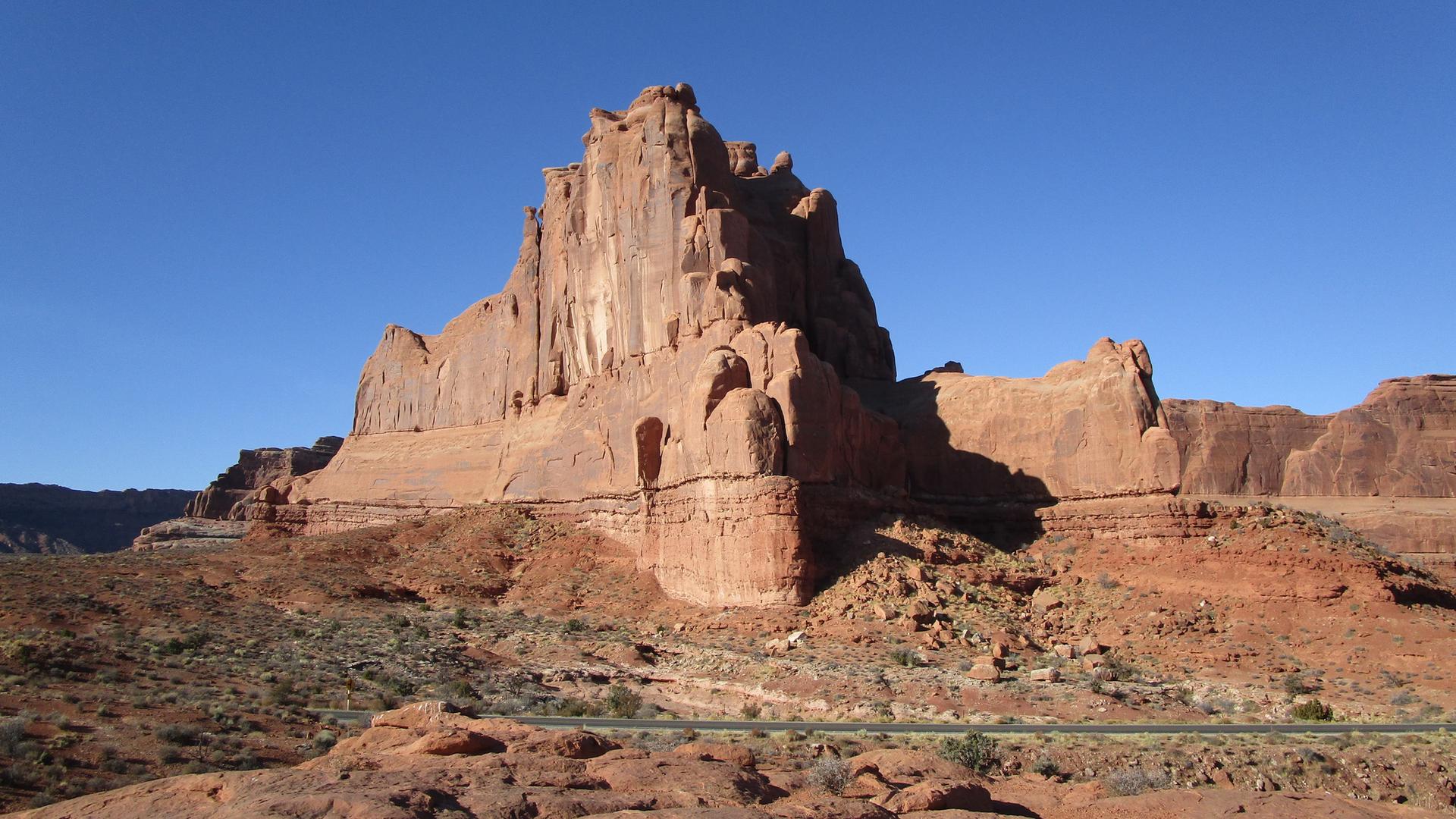 Grand red rock formation dominates a desert landscape under clear blue sky.