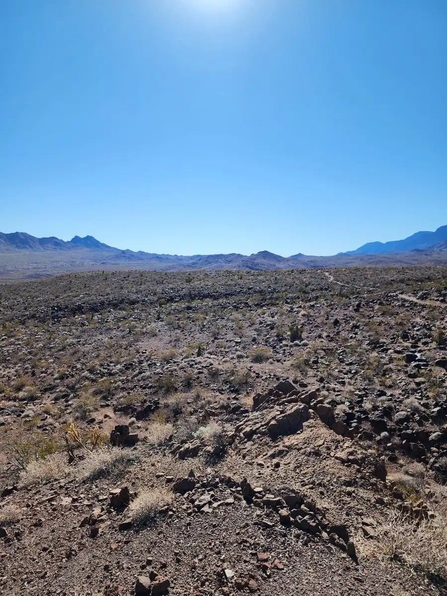 Rocky desert terrain under a bright blue sky with sun glare and distant mountains. - 601 Trail to 701 Trail Loop