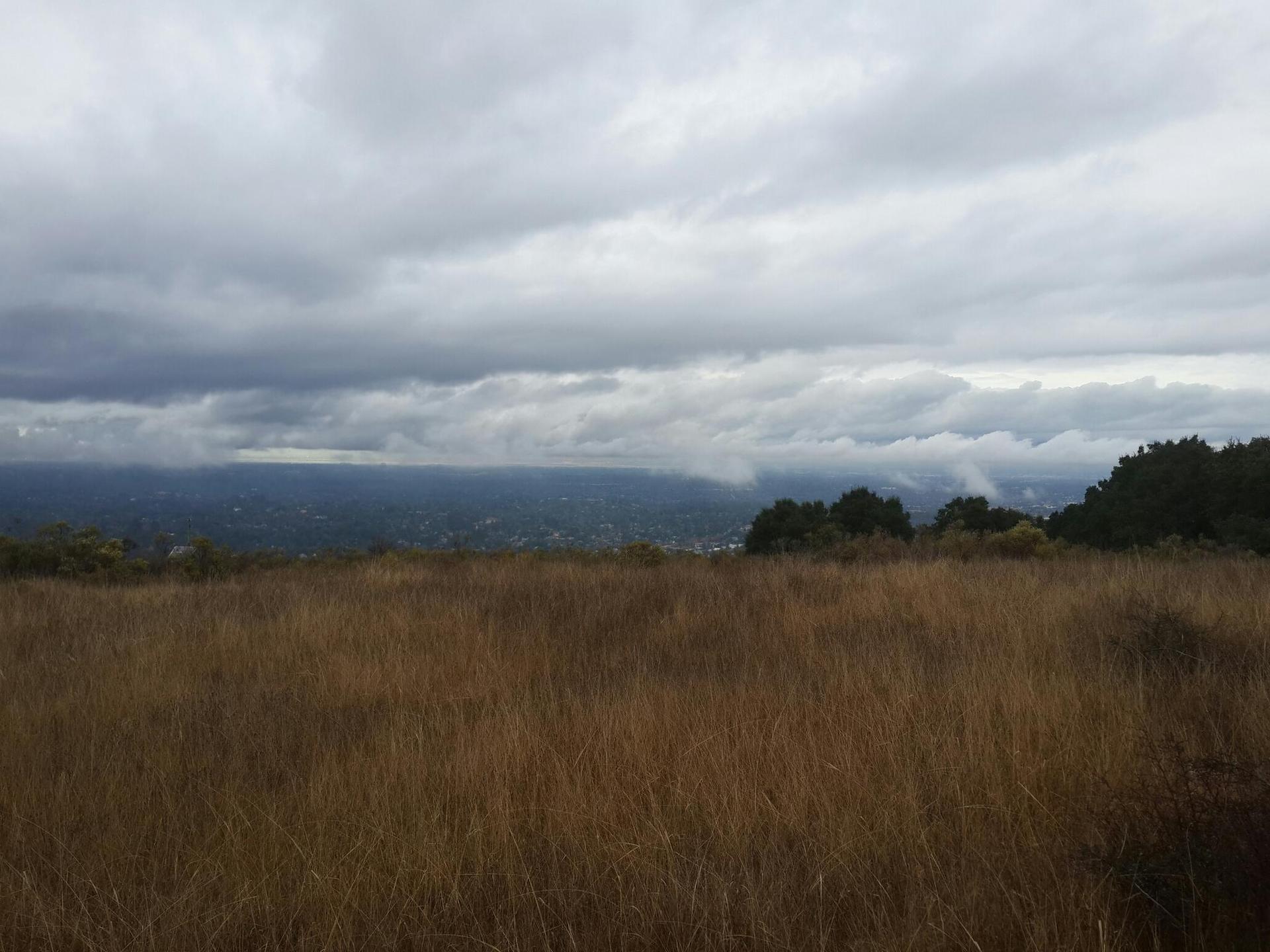 Overcast sky above a dry grassy field overlooking a distant valley.