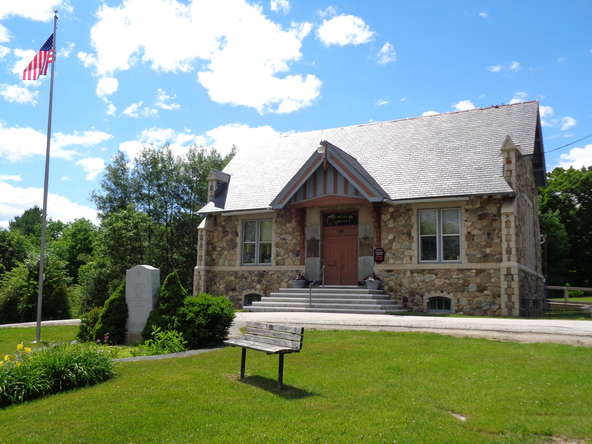 Stone building with flagpole, American flag, and bench on a sunny day.