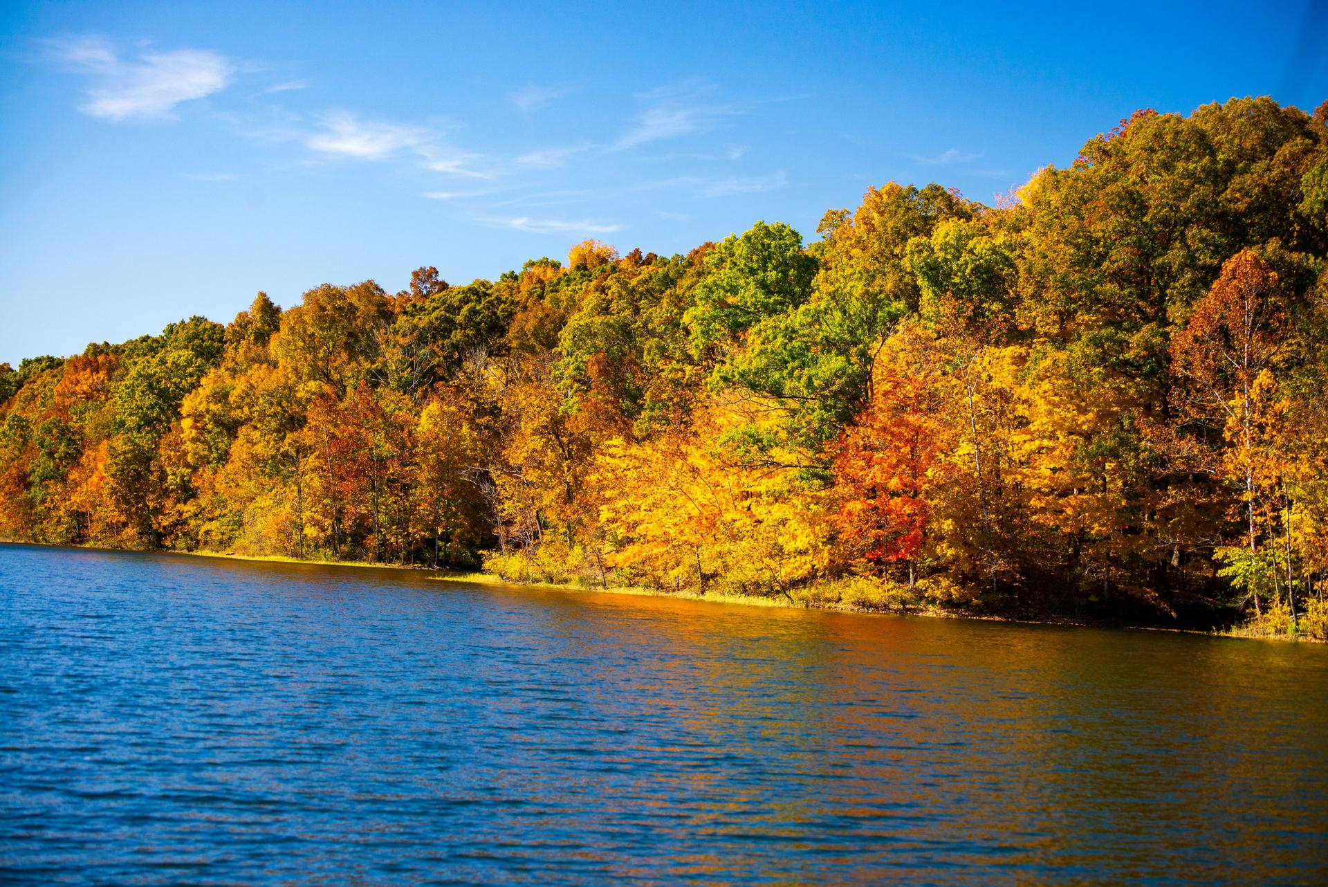 Blue lake reflecting vibrant autumn trees under a clear, sunny sky.