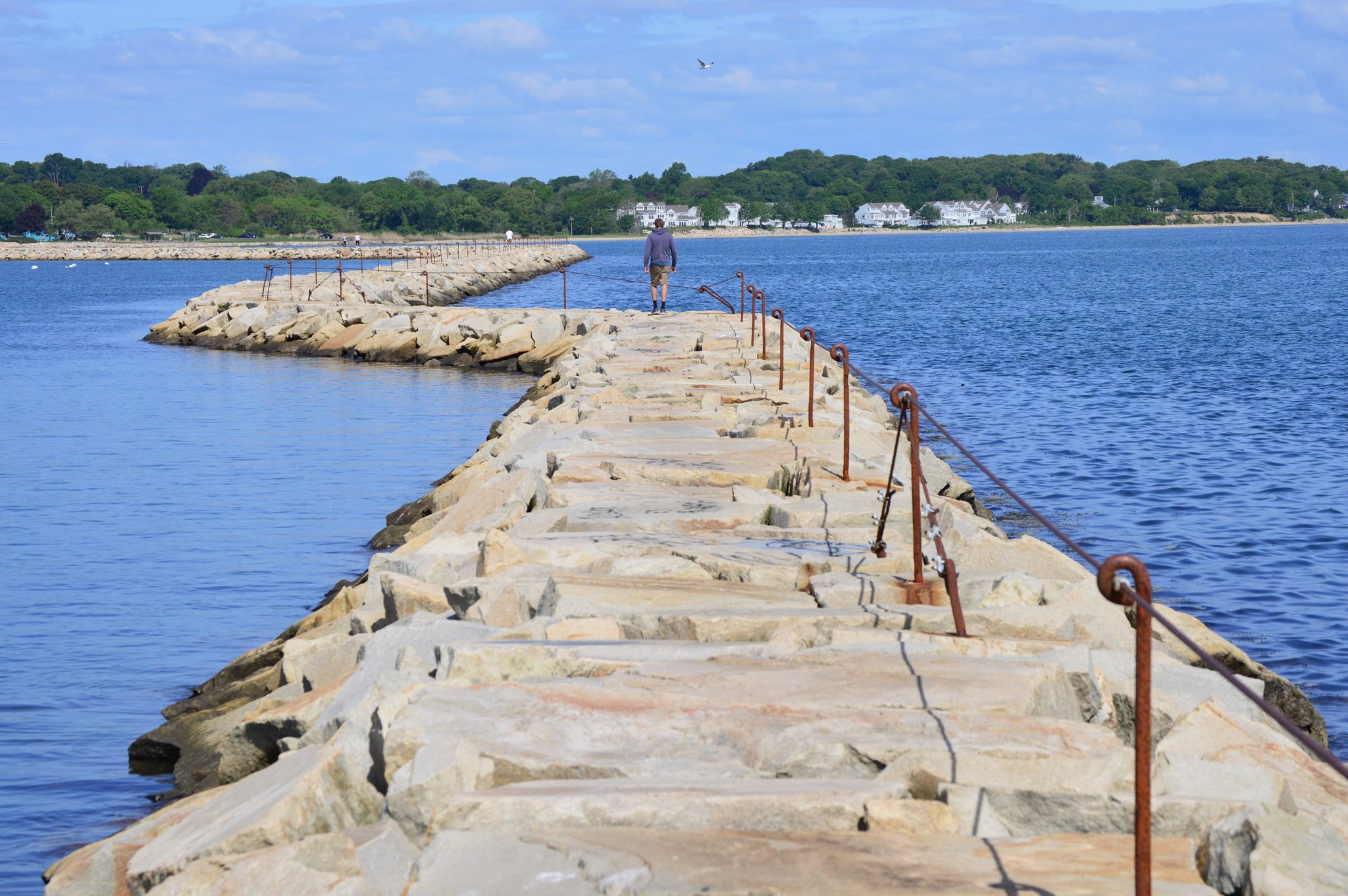 A person walks on a long stone jetty extending into calm blue water. - Plymouth Breakwater loop from Plymouth