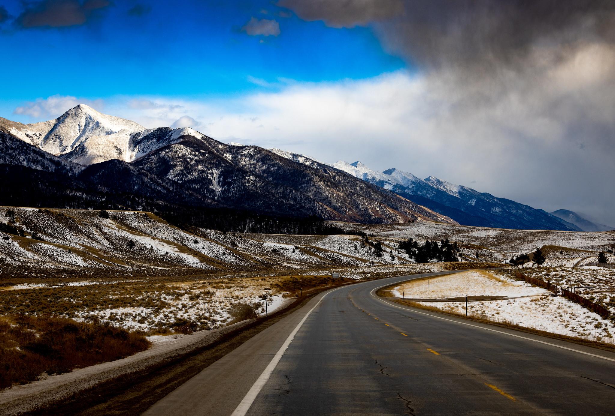 Winding road leads to snow-capped mountains under dramatic, partly cloudy sky.