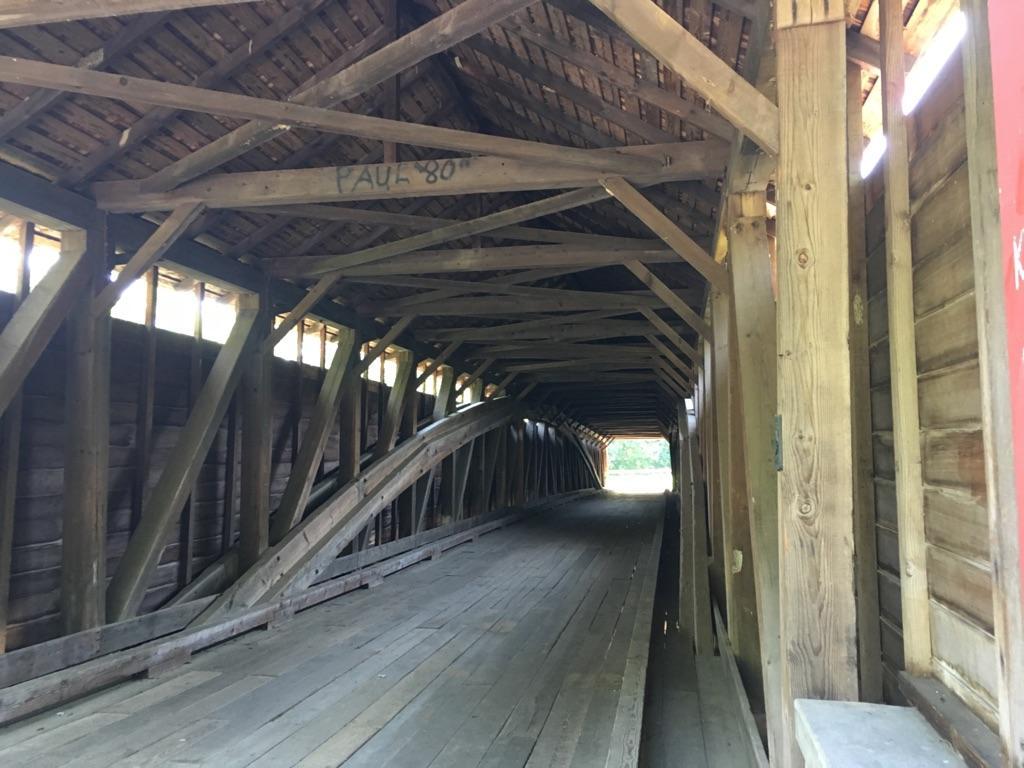 Inside a long, old wooden covered bridge with visible beams and dim light.
