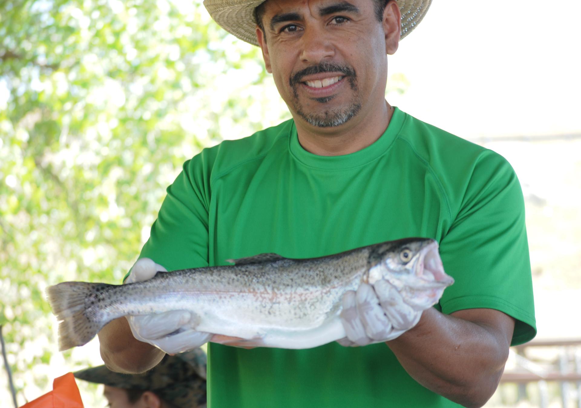 Smiling man in straw hat and green shirt holding a large fish outdoors.