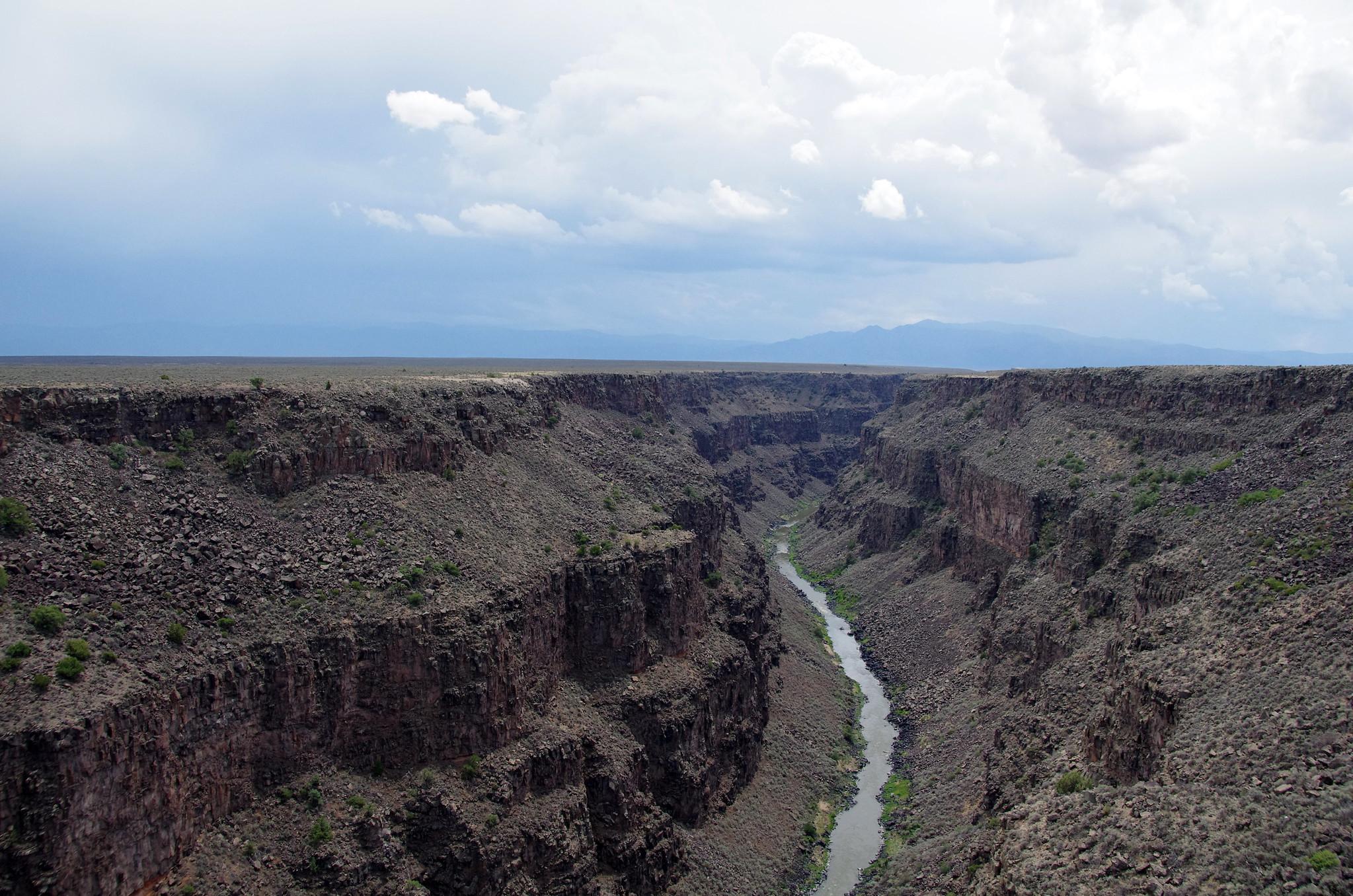 Wide view of a deep, rocky canyon with a winding river under cloudy skies.