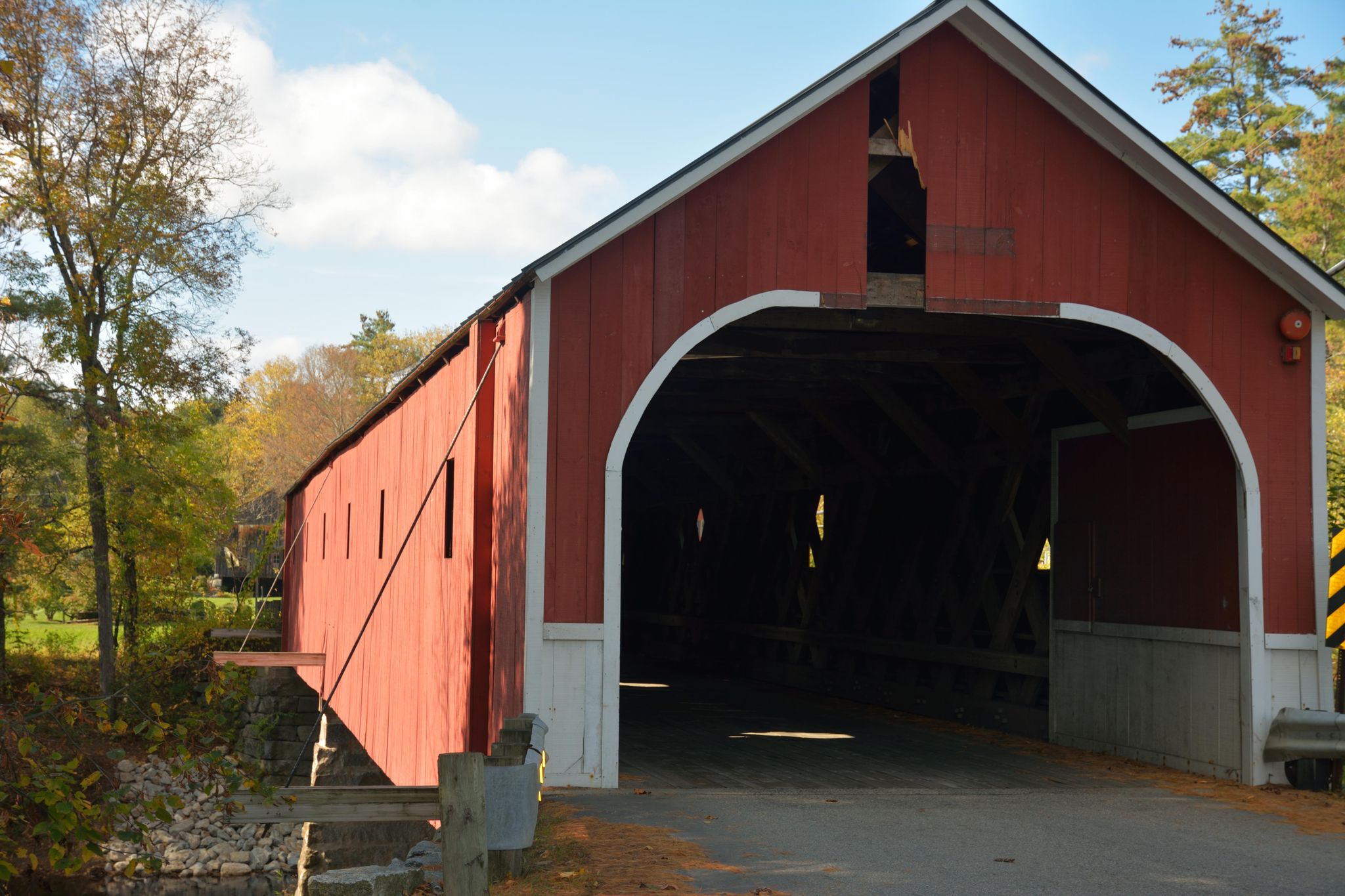 A red covered bridge with autumn trees under a bright sky. - Ashuelot Rail Trail Loop