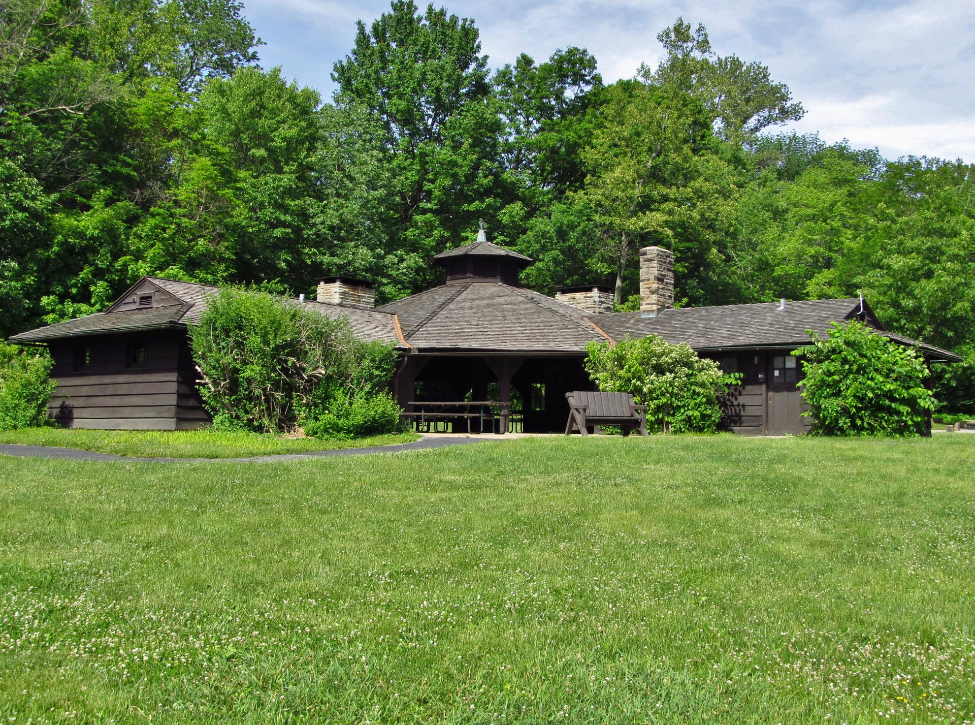 Large dark wooden building with a cupola, surrounded by green lawn and forest.