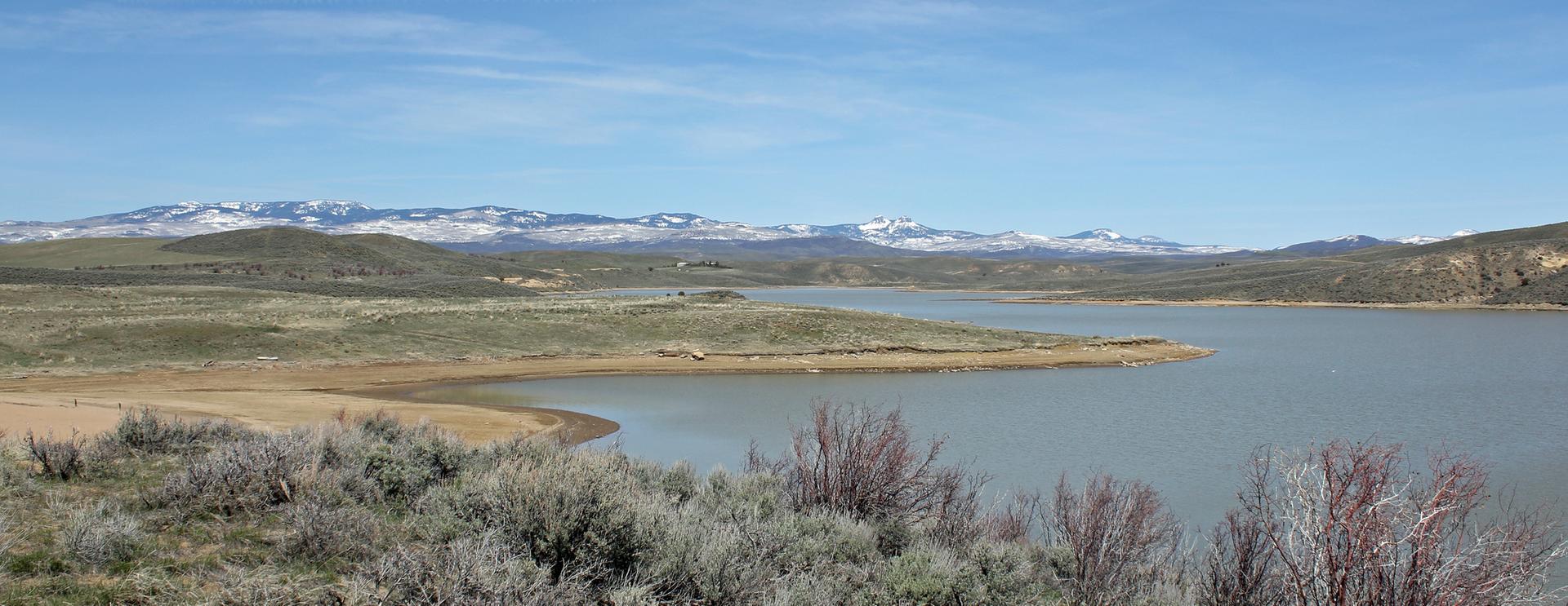 Vast lake with arid hills, distant snowy peaks, and clear blue sky.