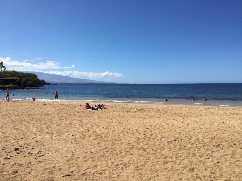Sunny beach with people sunbathing and wading in the clear blue ocean.