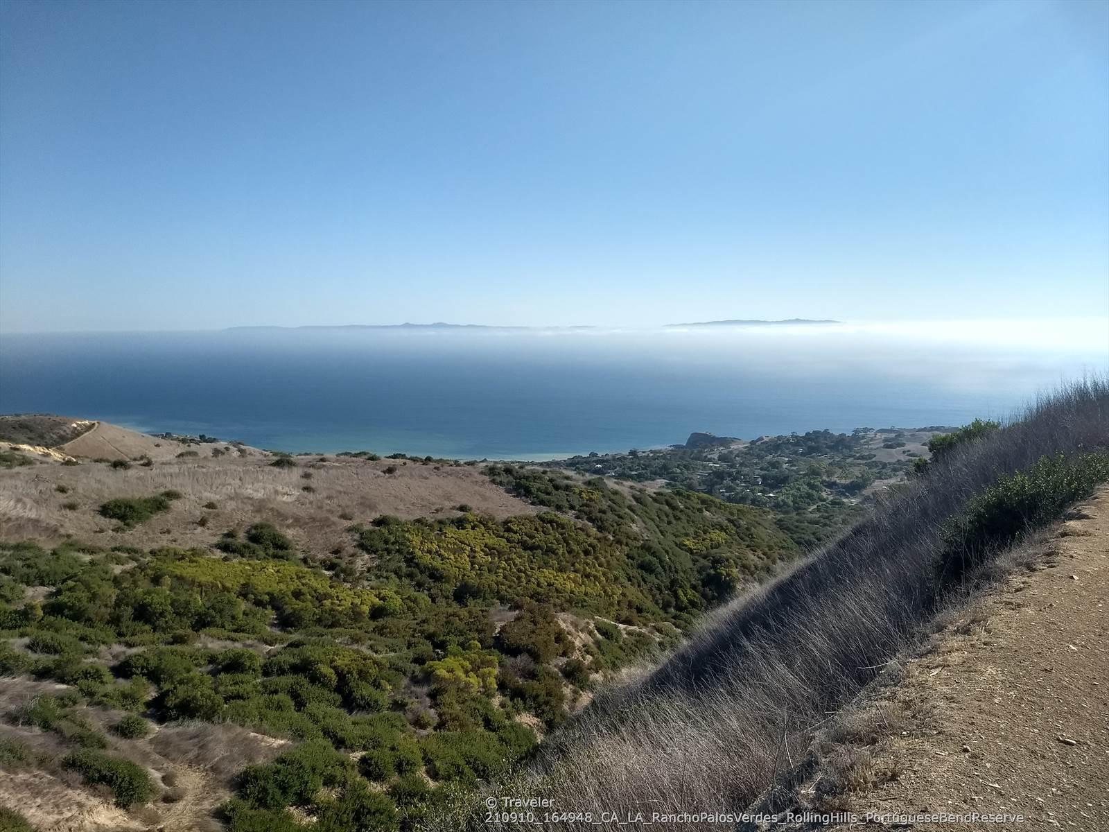 Panoramic view of a vast blue ocean from a dry, green hillside.