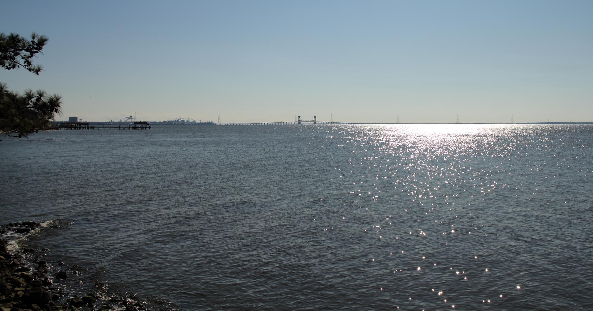 Sparkling sun reflects on a wide body of water with distant structures.