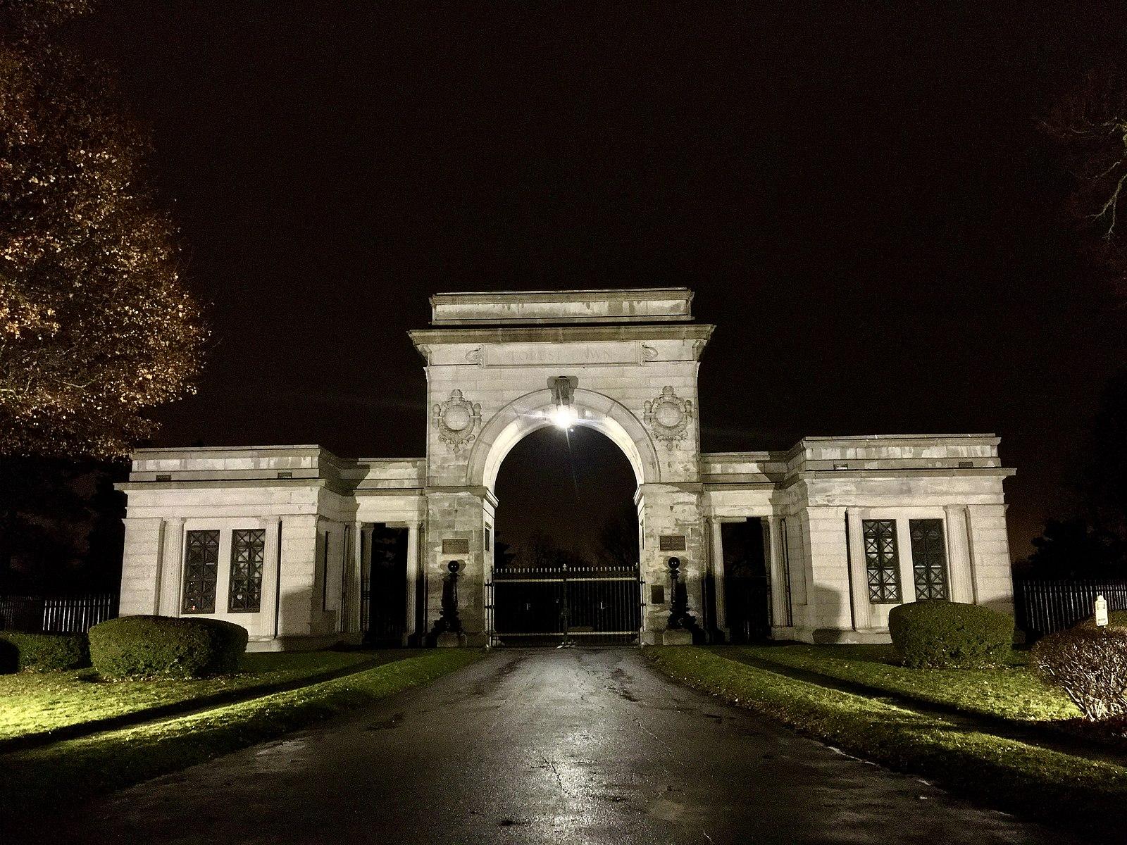Ornate stone archway entrance illuminated by spotlights at night.