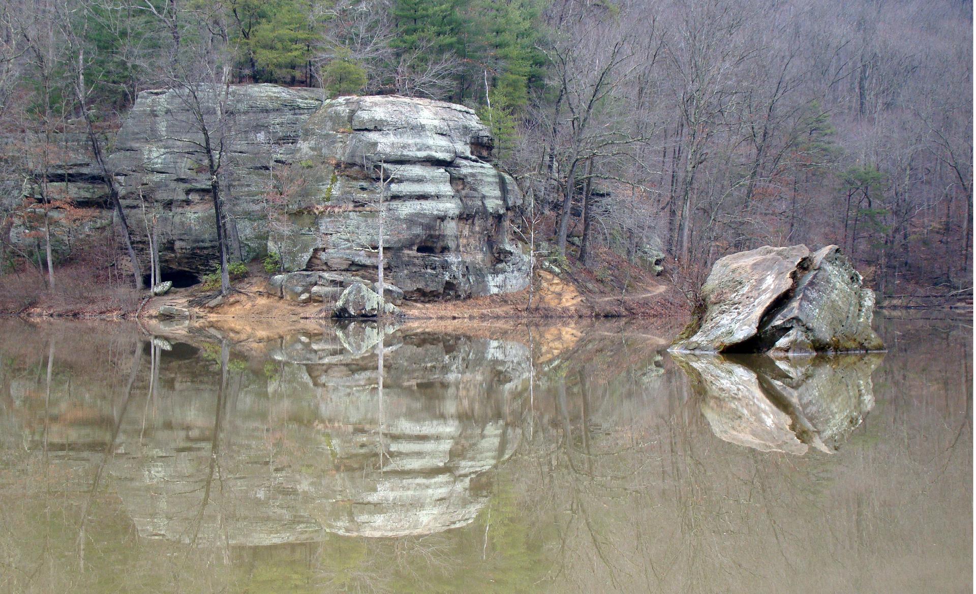 Large rock formations reflected in a calm lake with bare trees.