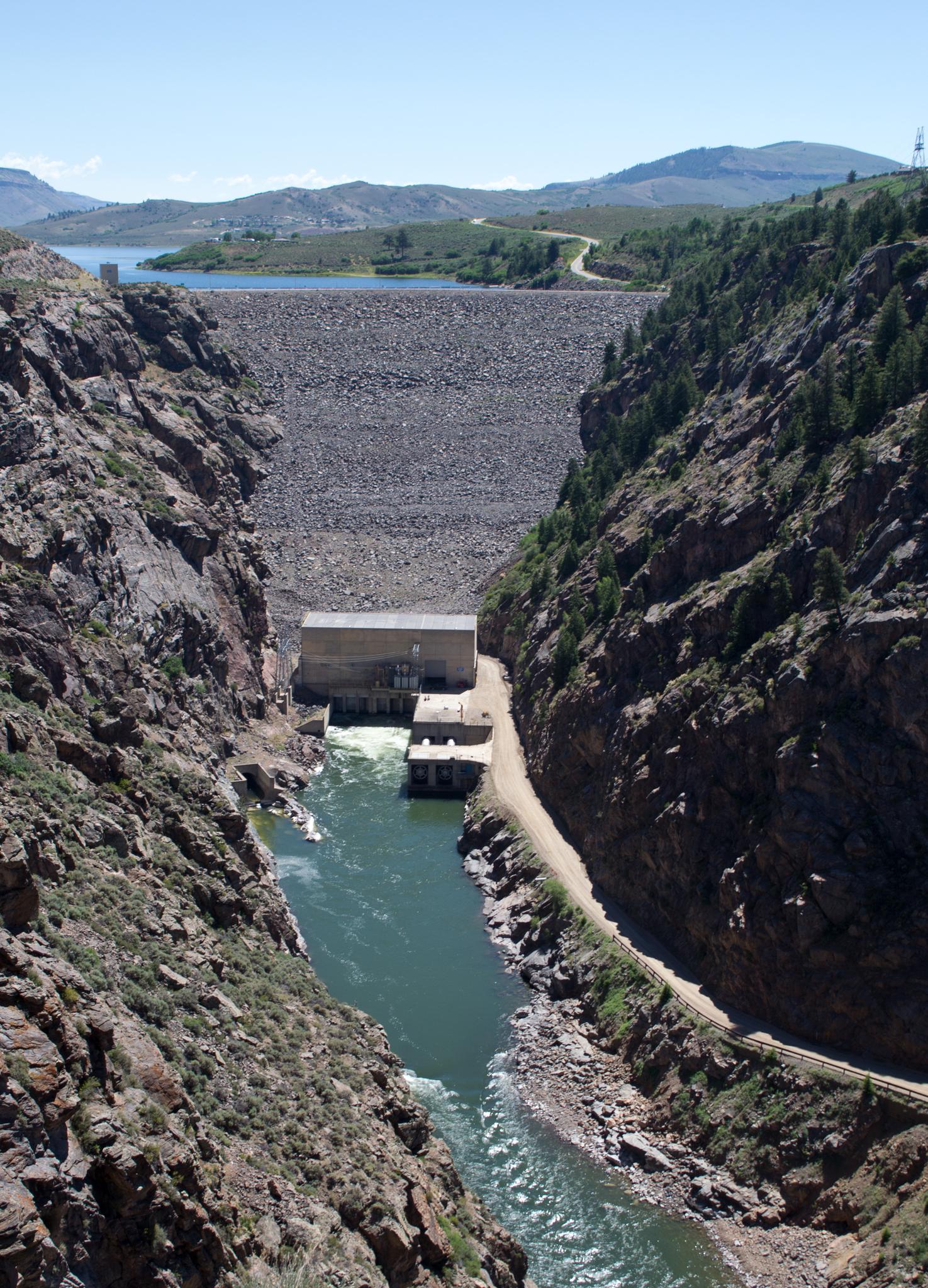 A large dam and river in a deep, rocky canyon on a sunny day.