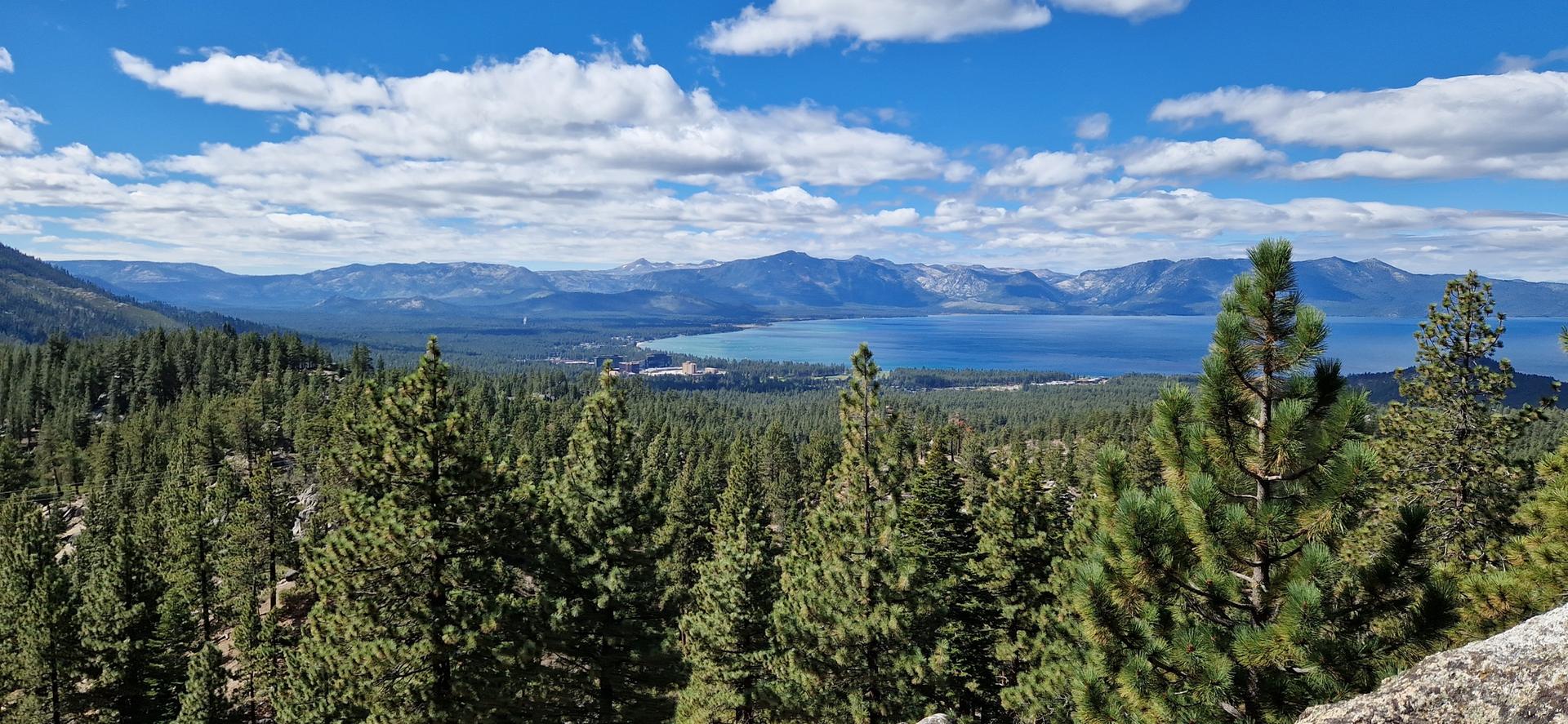 Panoramic view of a vast blue lake surrounded by forests and mountains.