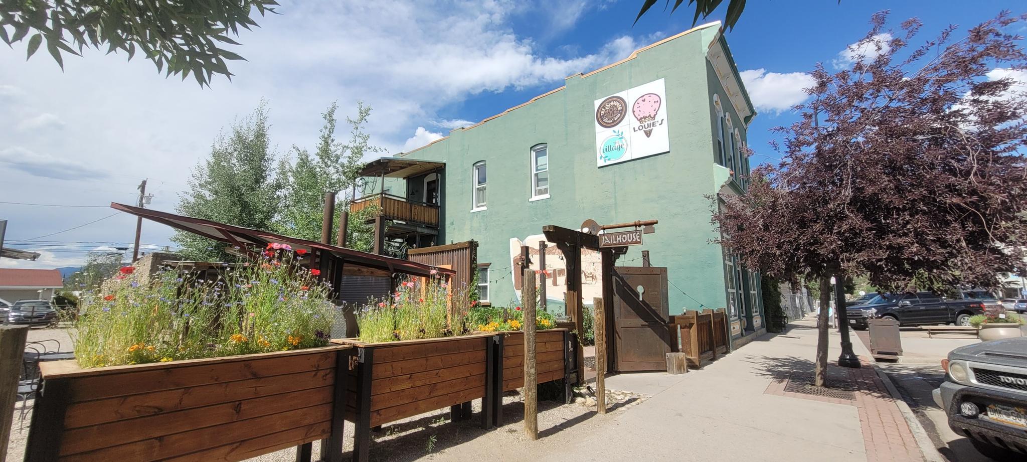 Green building with outdoor patio and planters under bright daylight.
