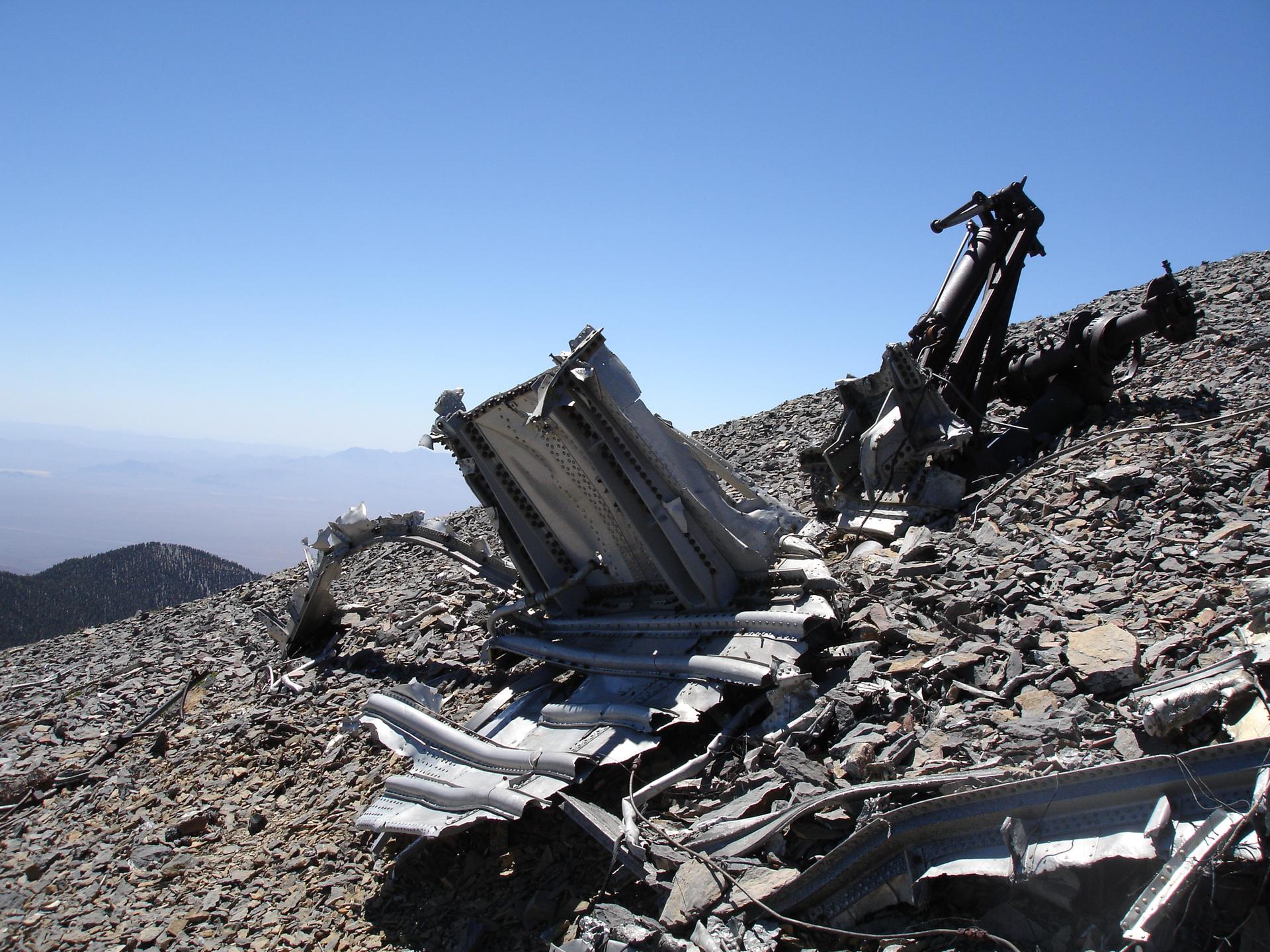 Metal wreckage scattered on a rocky mountain slope under a clear blue sky.