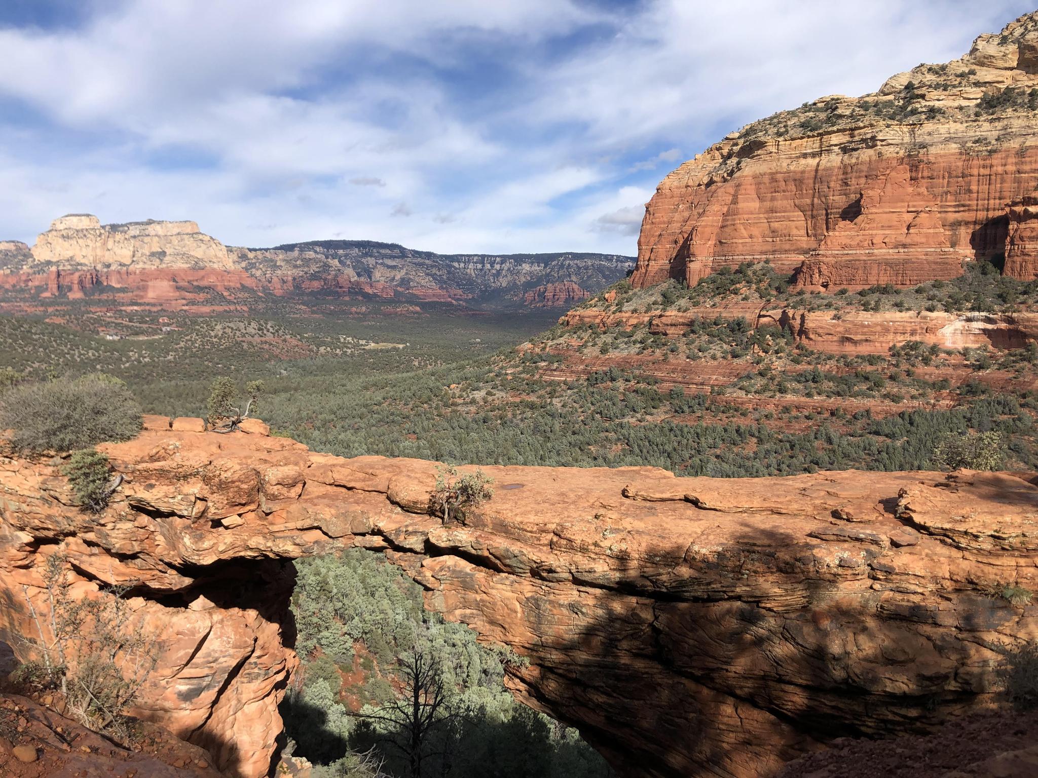 Natural red rock arch overlooking a vast valley with distant mountains.