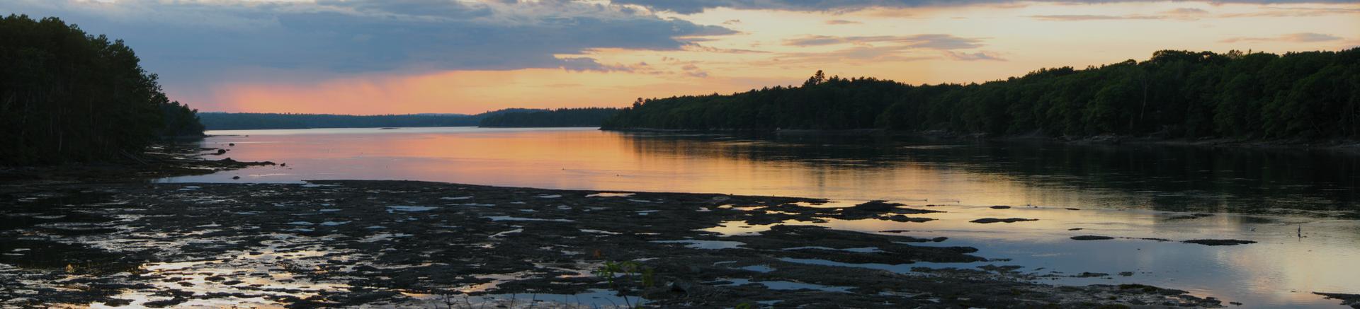 Panoramic view of a wide river at sunset, reflecting colorful sky.