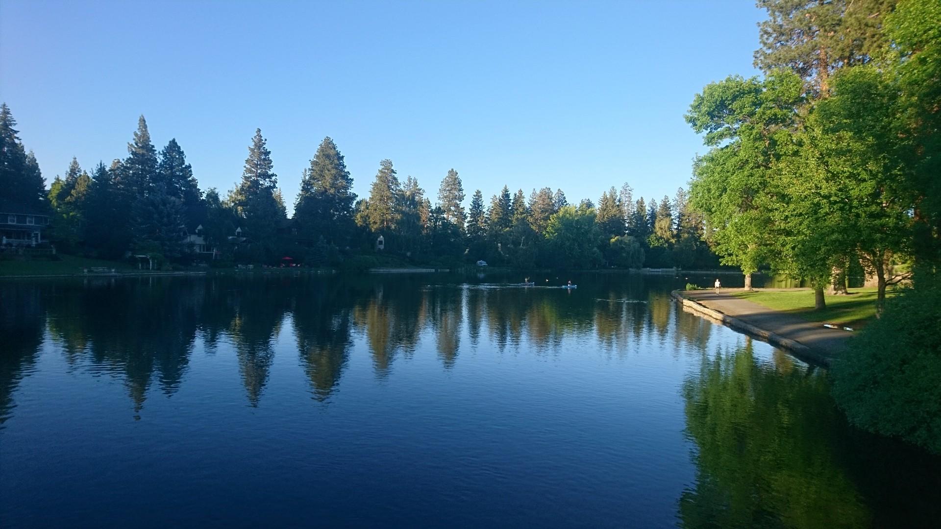 Sunny day over a calm lake with green trees reflecting in the water.