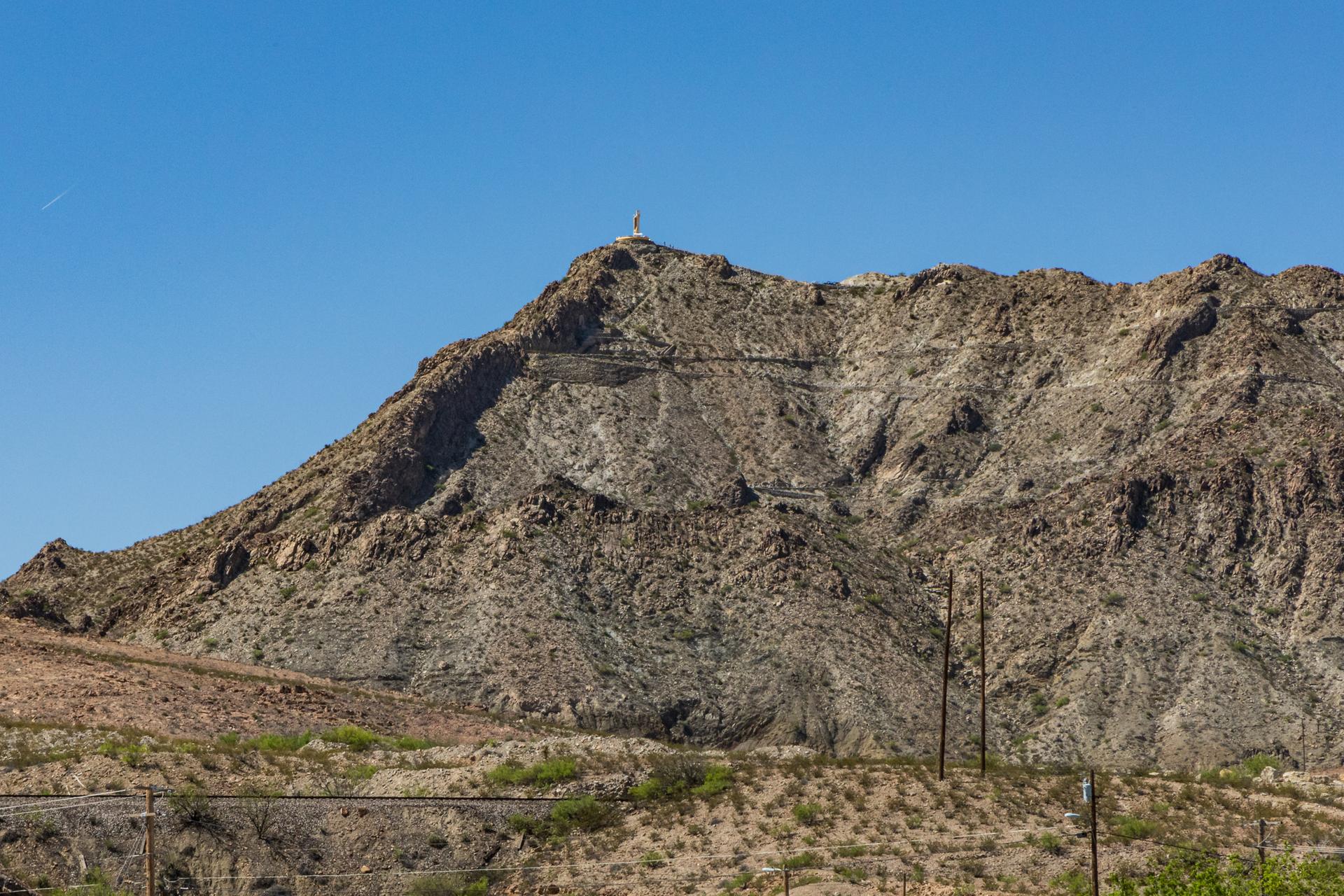 Rugged desert mountain with a small structure on its peak under a clear sky.