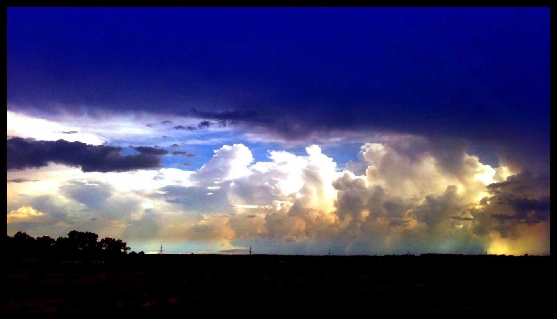 Dramatic sky with dark storm clouds and bright, illuminated cumulus clouds.