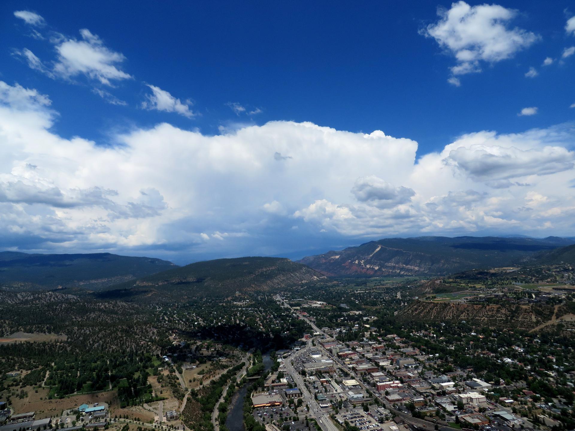 Aerial view of a town, river, and mountains under a dramatic cloudy sky.