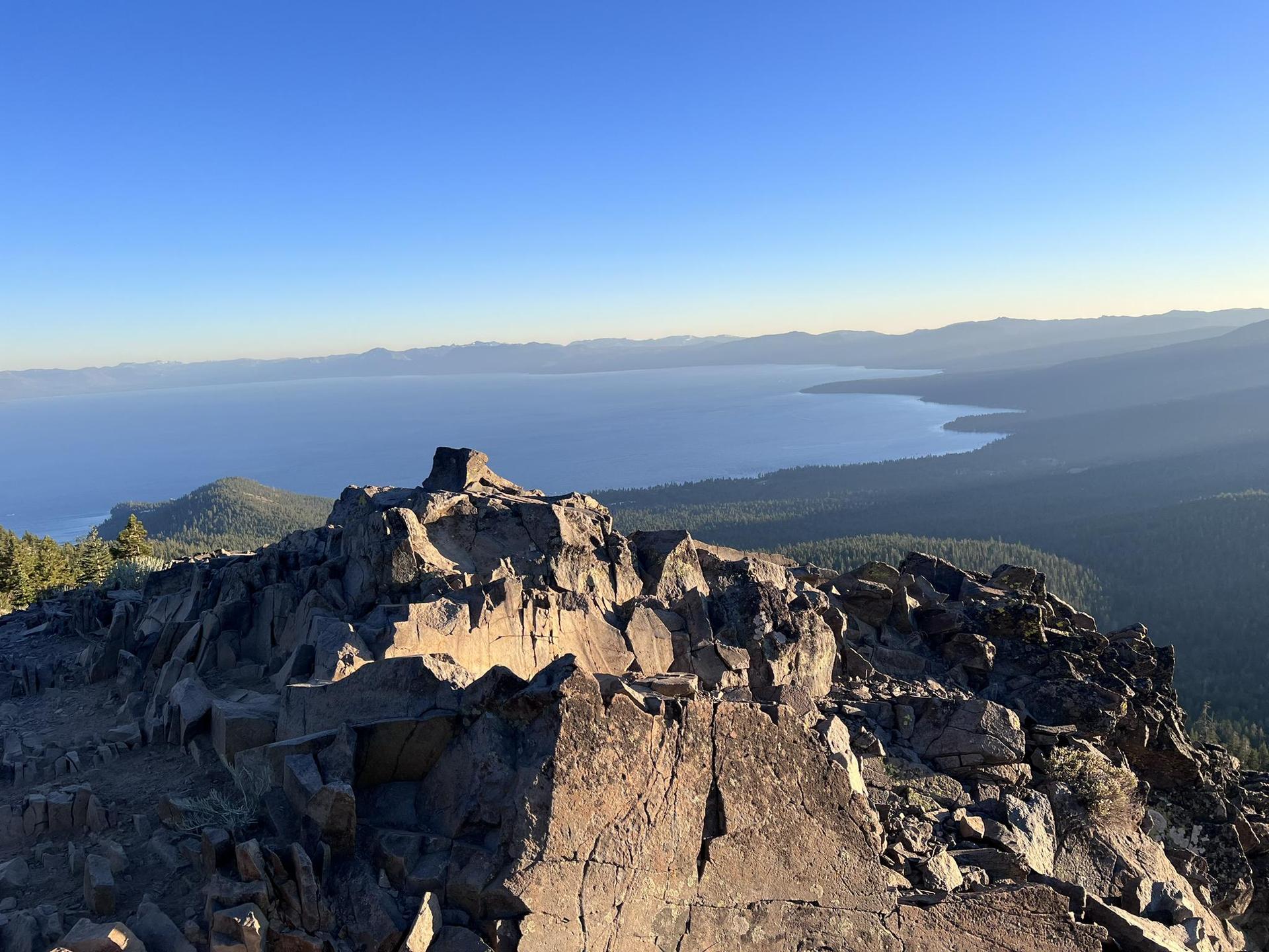 Rugged mountain peak overlooking a vast blue lake at golden hour.