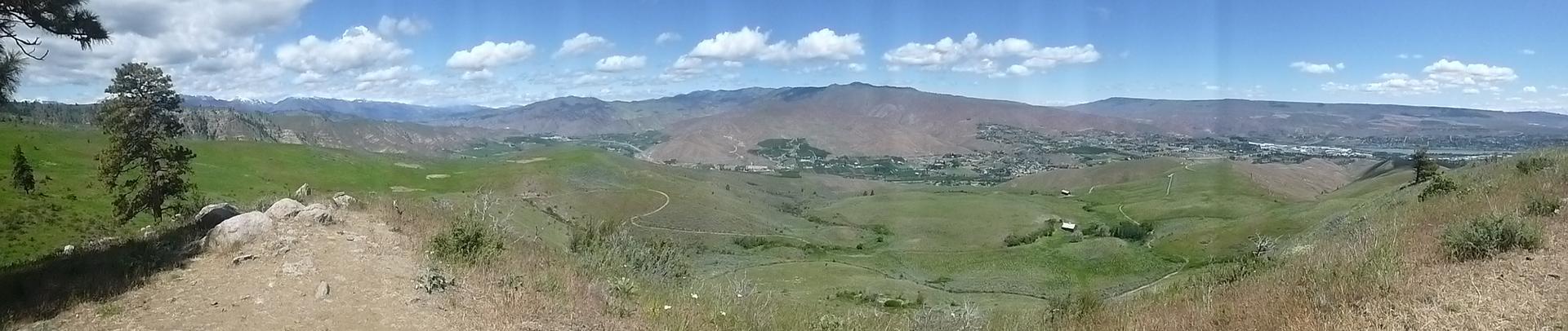 Panoramic view of a vast green valley under a bright, cloudy sky.