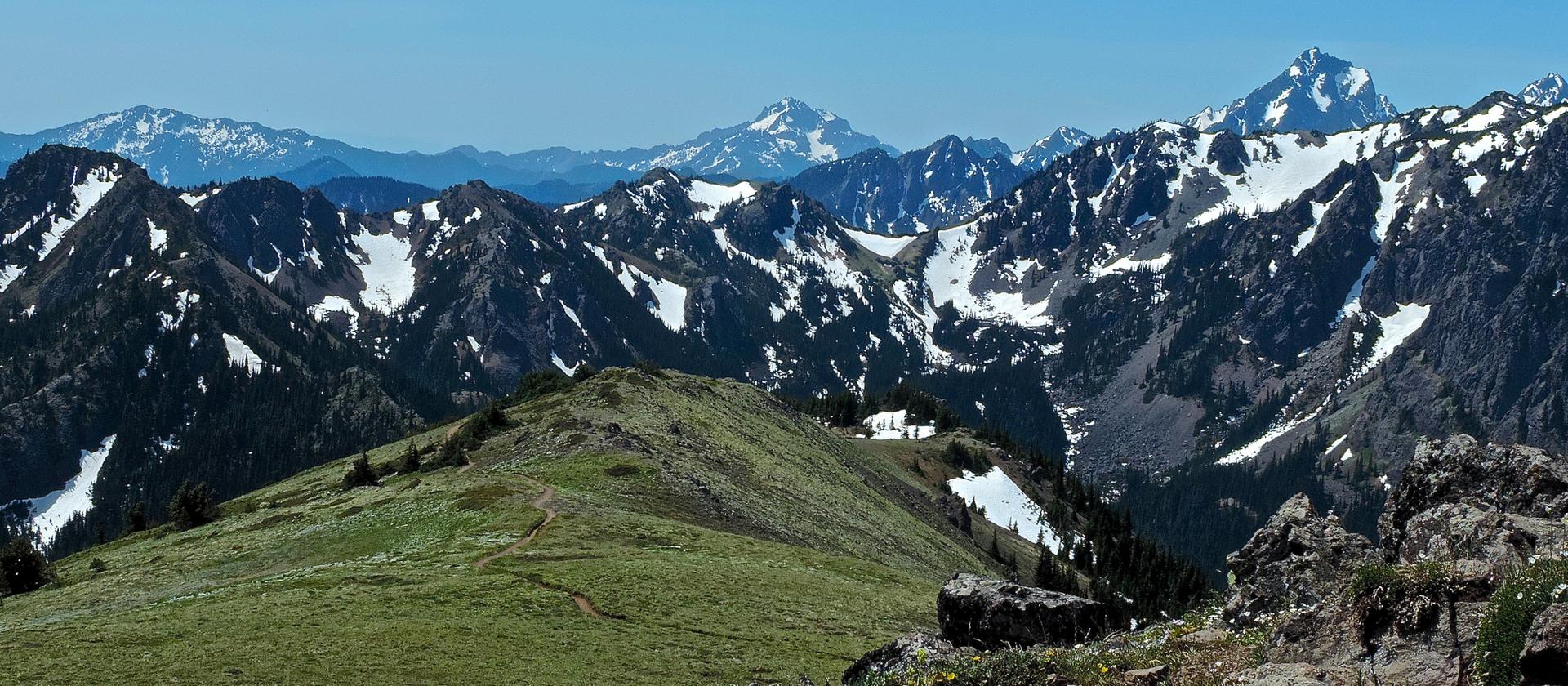Sunny view of rugged, snow-capped mountains and a green foreground ridge.