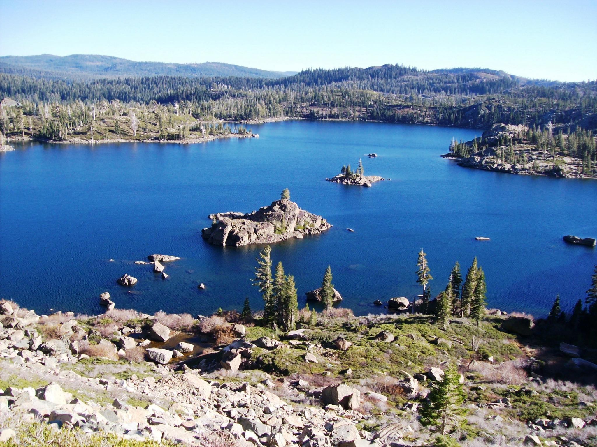 Bright blue lake with rocky islands surrounded by green forested hills.