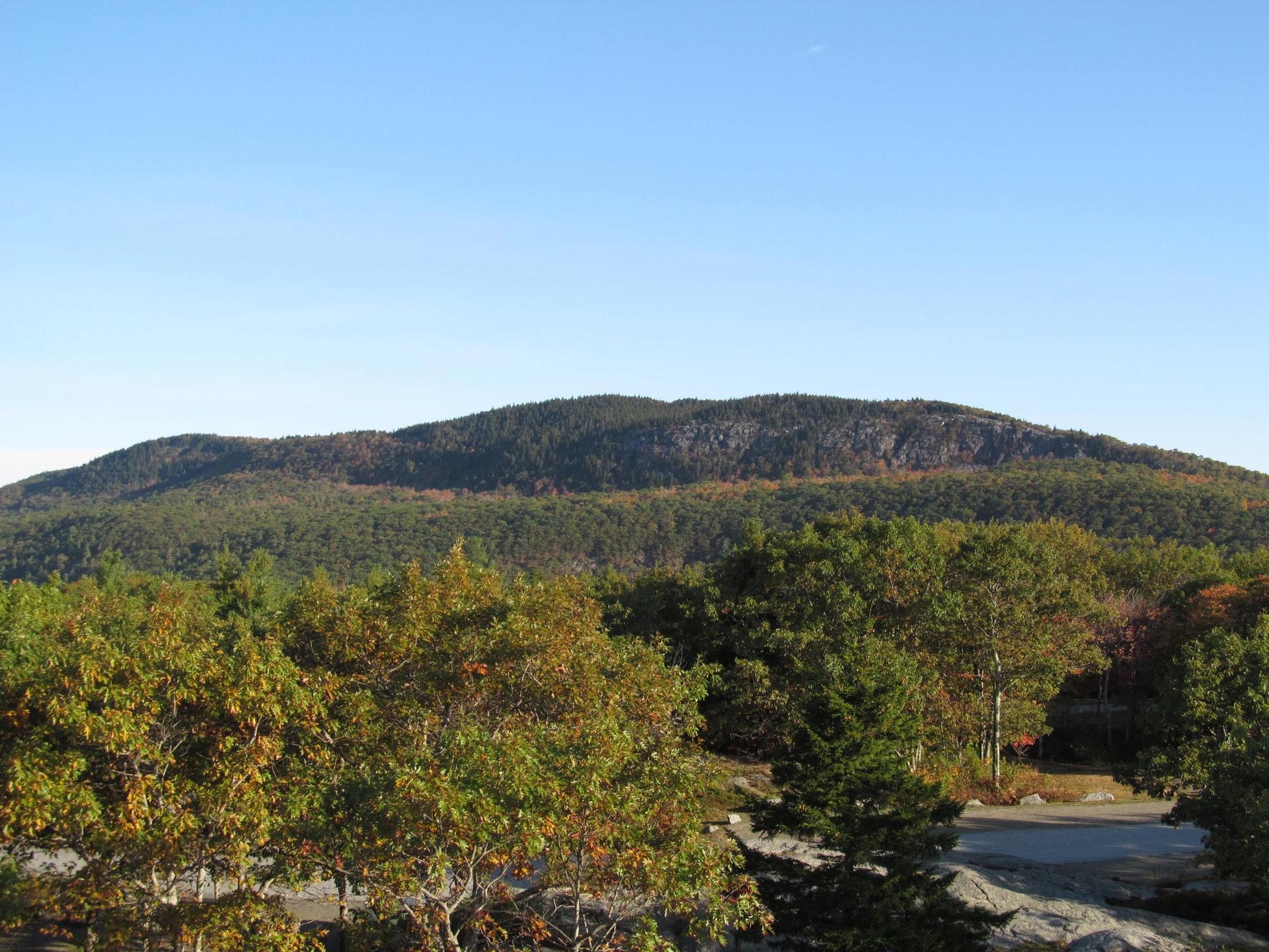 Lush green and autumn-colored trees cover rolling mountains under a clear sky.