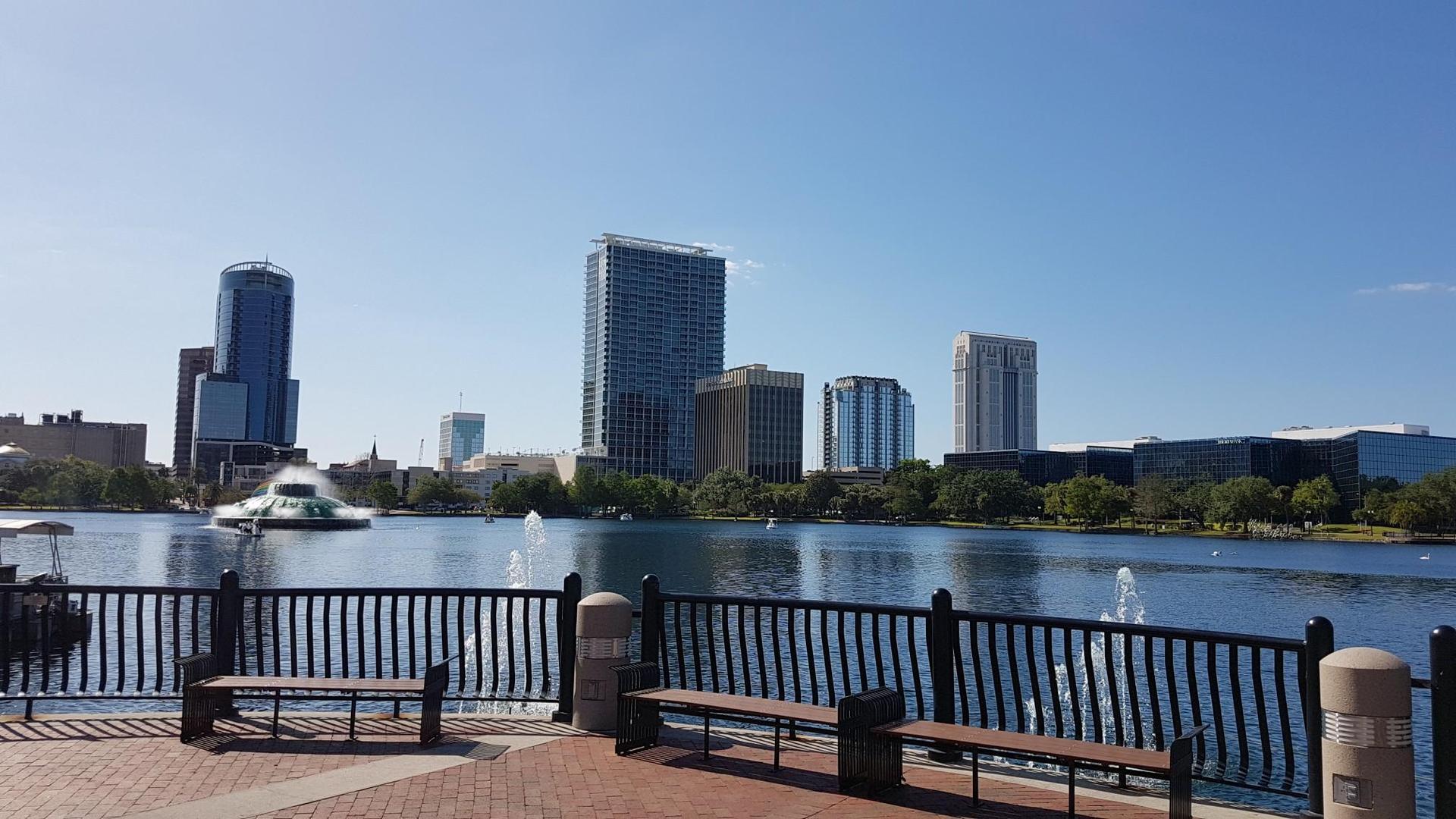 City skyline across a lake, seen from a waterfront promenade with benches.