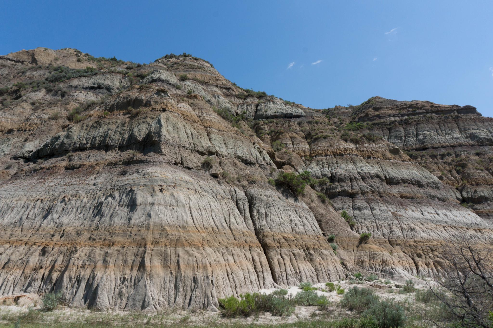 Steep, multi-colored layered rock face under a clear blue sky.