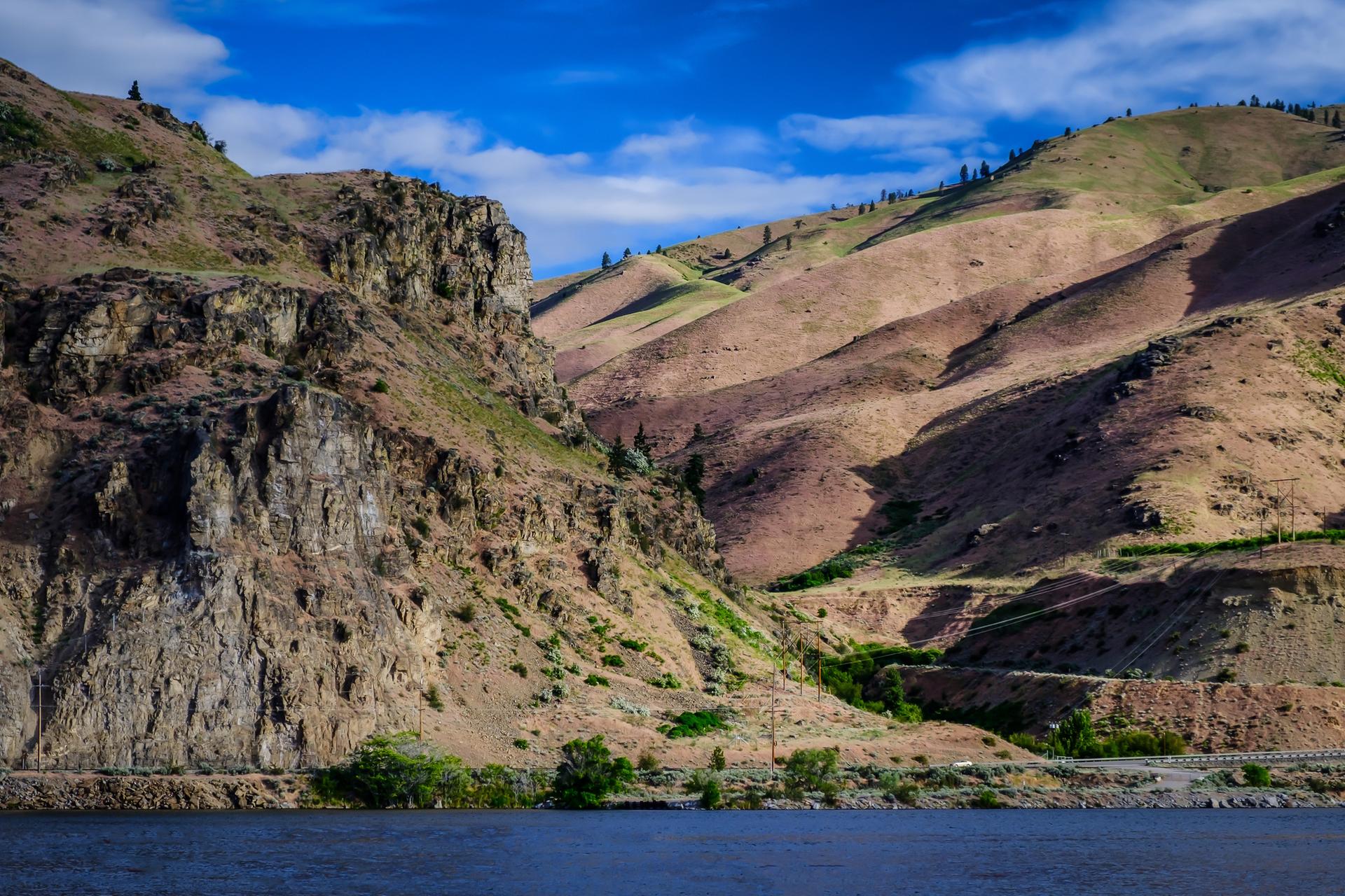 Steep rocky and grassy hills rise from a dark blue body of water.