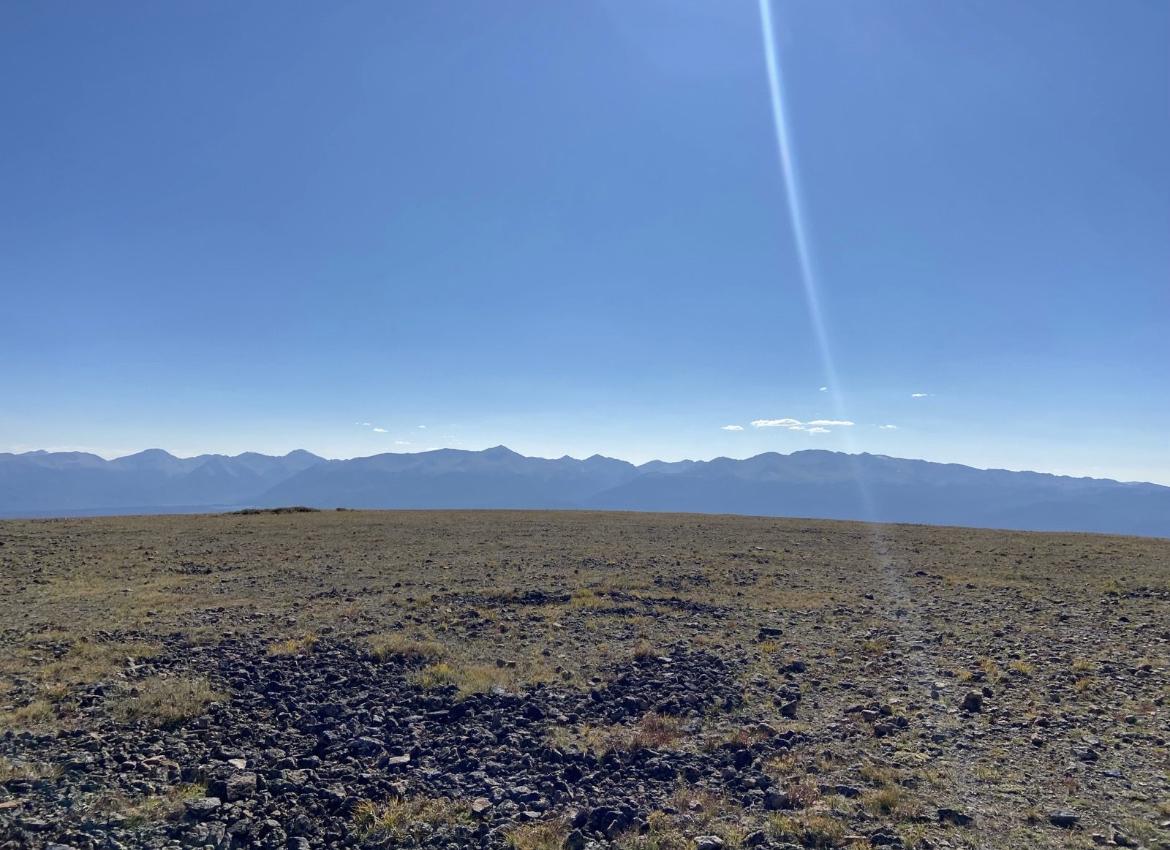 Rocky, barren high-altitude landscape under a bright, clear sky with distant mountains.