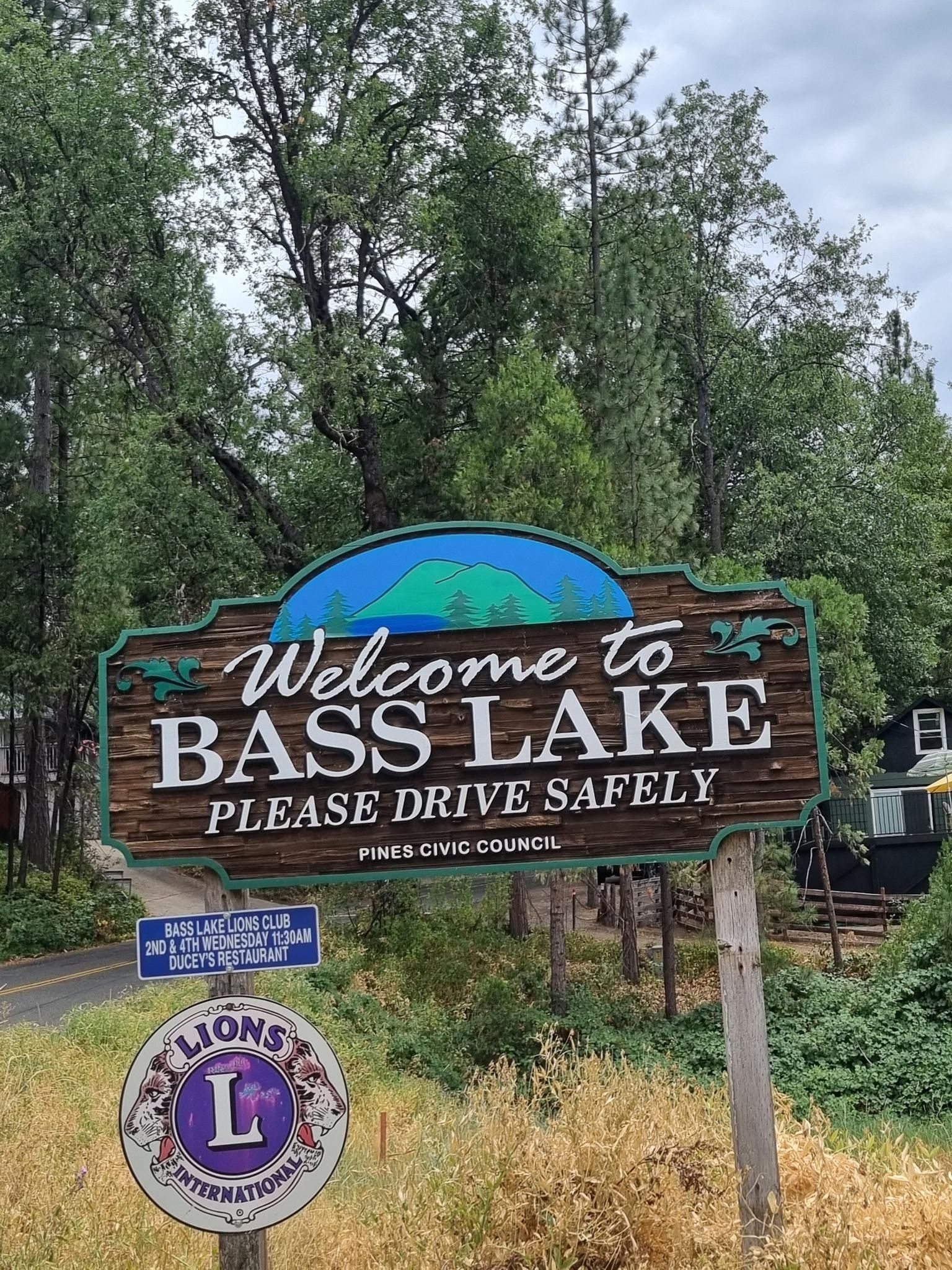 A rustic welcome sign and Lions Club emblem among green trees and foliage. - Oakhurst, California to Bass Lake loop