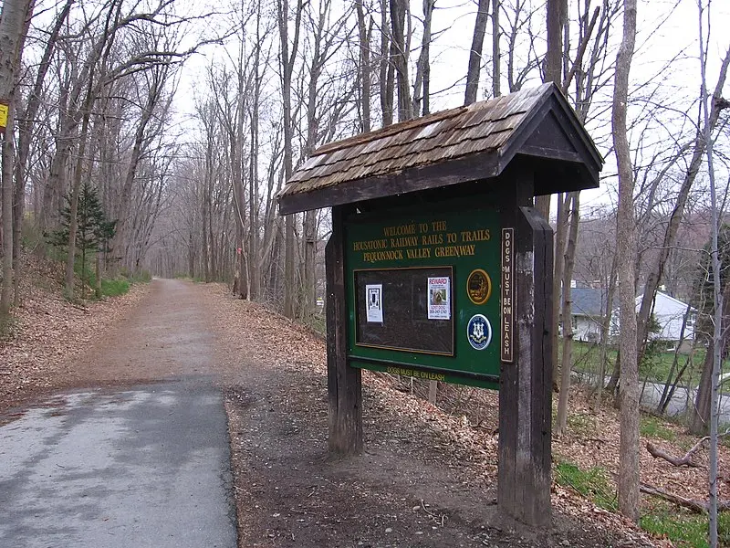 A wooden trail sign stands beside a dirt path through a bare forest.