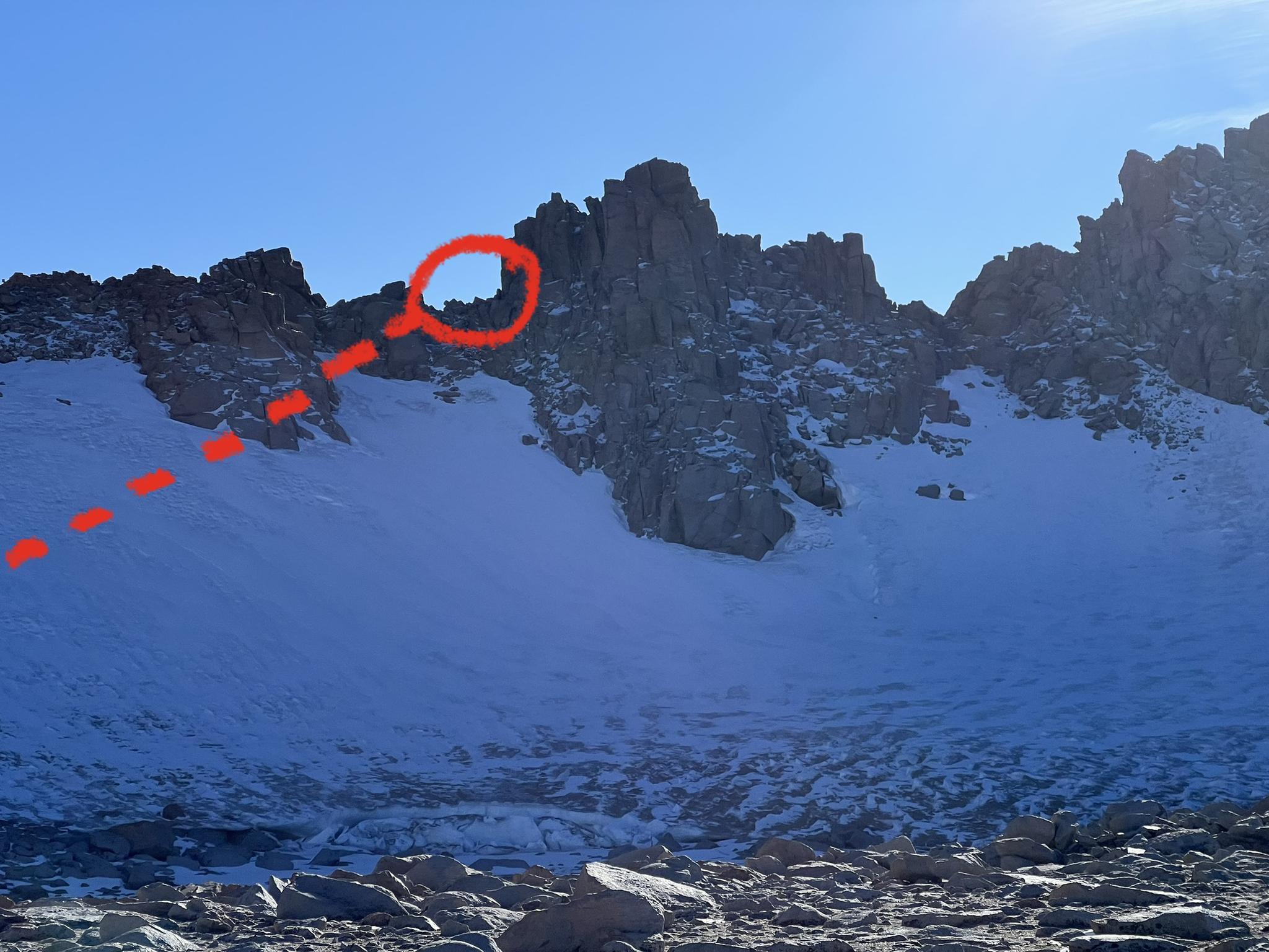 Jagged, snow-covered mountain peaks under a clear sky, with a red circle.