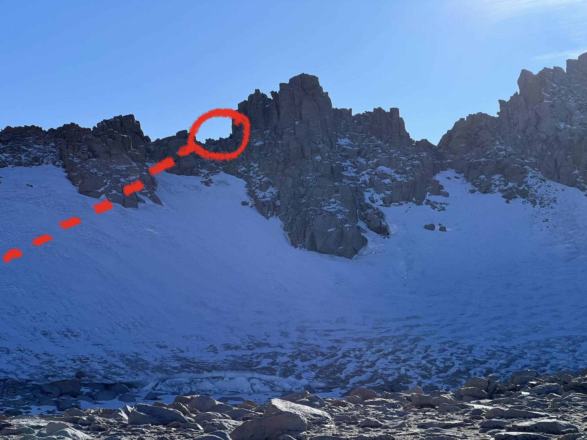 Jagged, snow-covered mountain peaks under a clear sky, with a red circle.