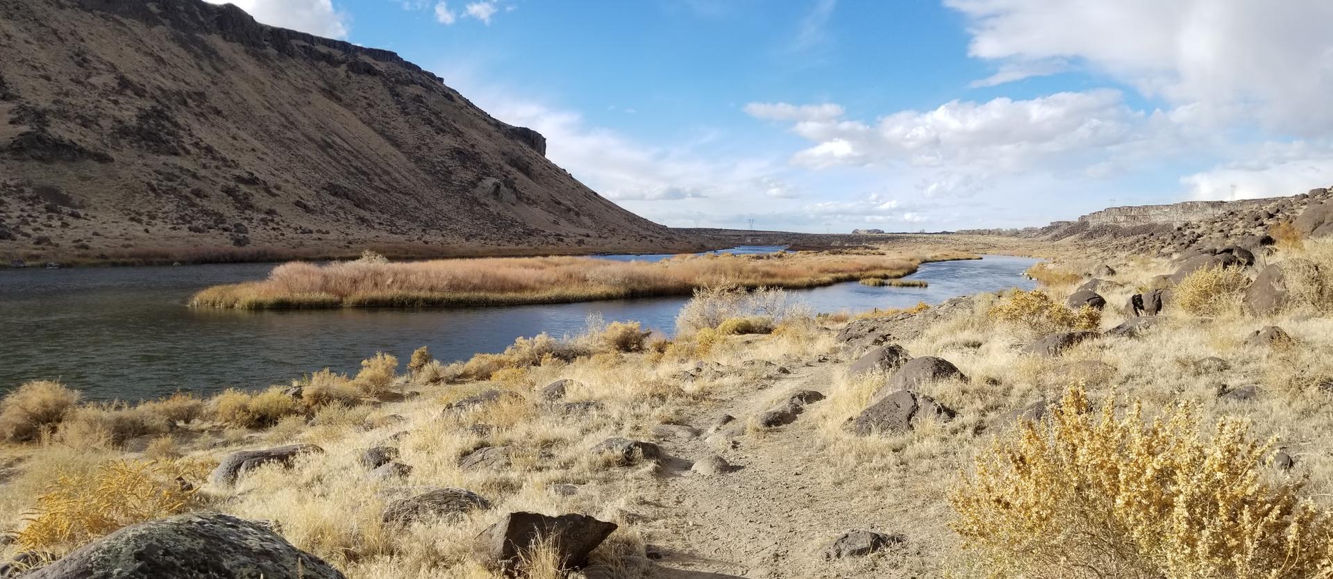Wide river flowing through a dry, rocky landscape under a blue sky.