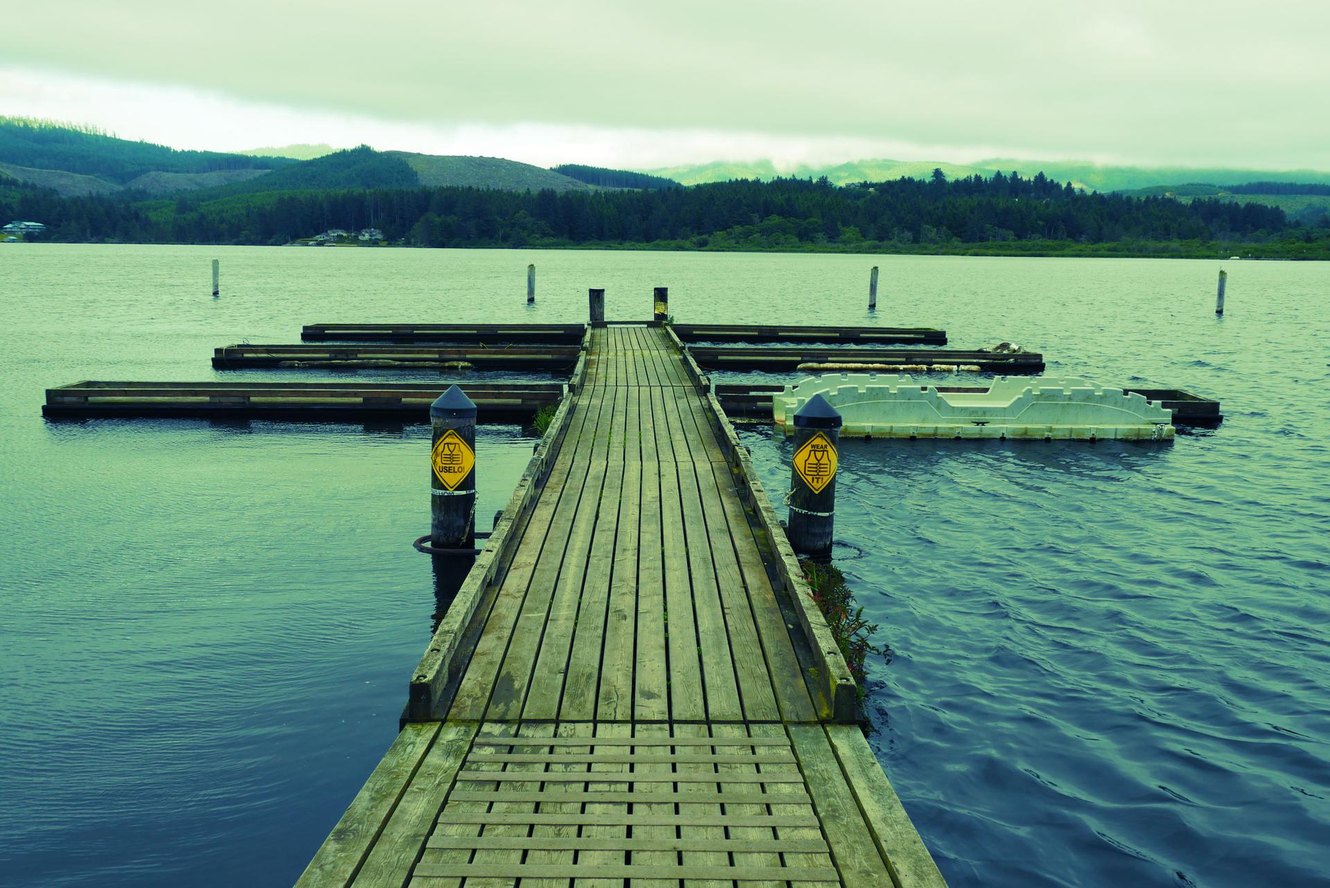 A wooden dock extends into a calm lake with distant forested hills.