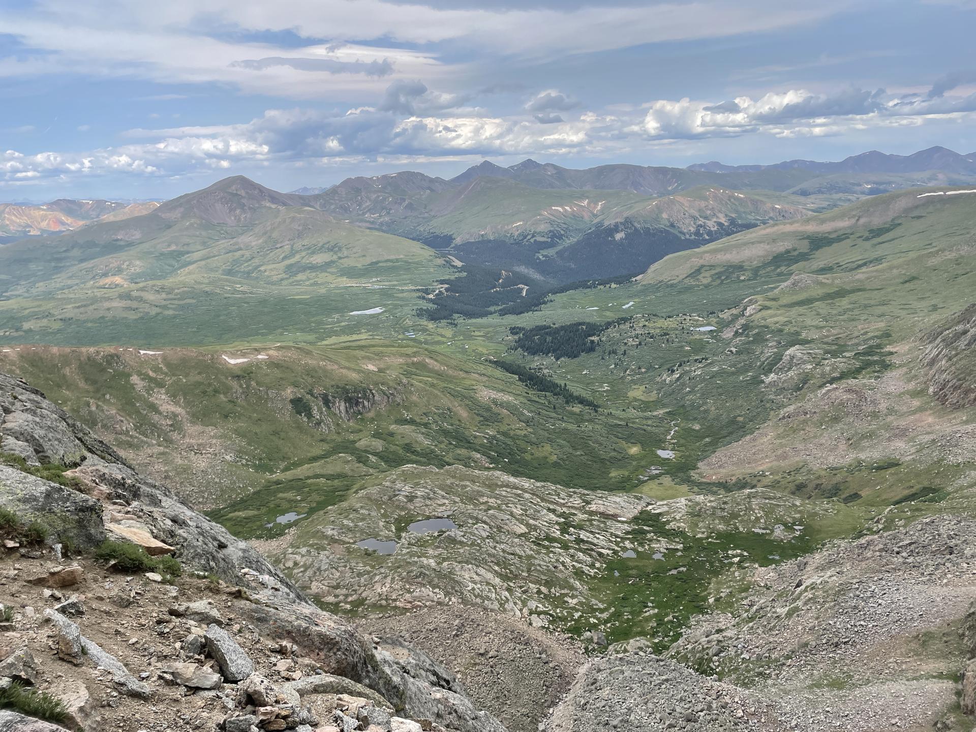 Panoramic view of a vast green mountain valley under a cloudy sky.