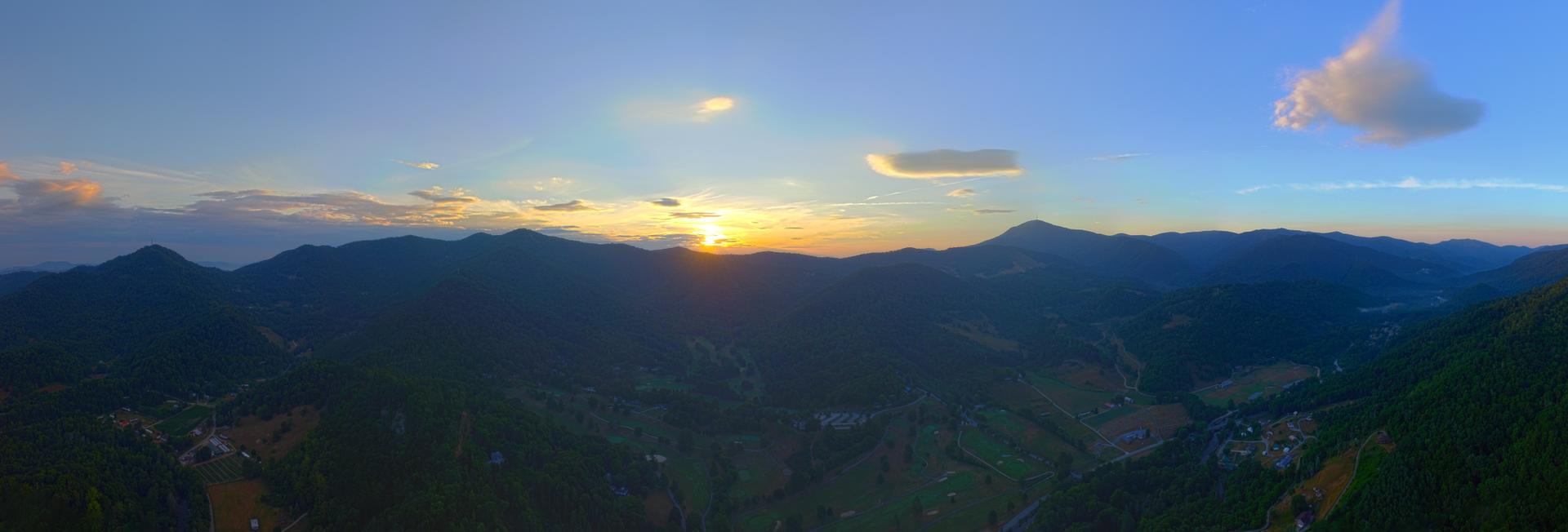 Panoramic sunset over dark, distant mountains and a valley.