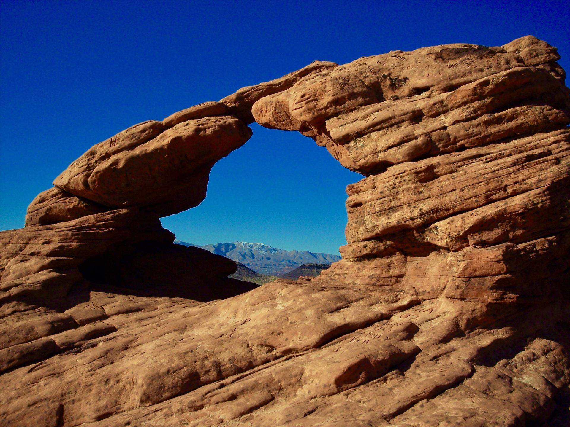 A natural rock arch frames distant mountains under a clear blue sky.