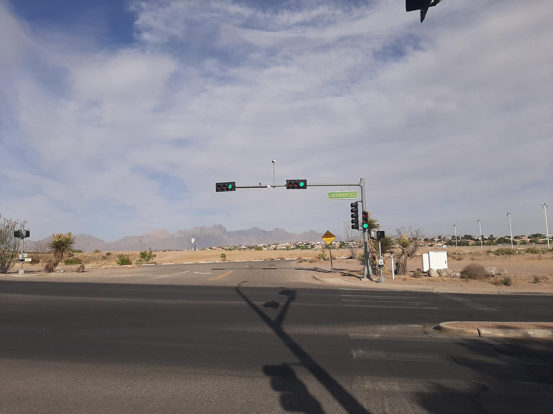 Desert road intersection with traffic lights and distant mountains under a cloudy sky.